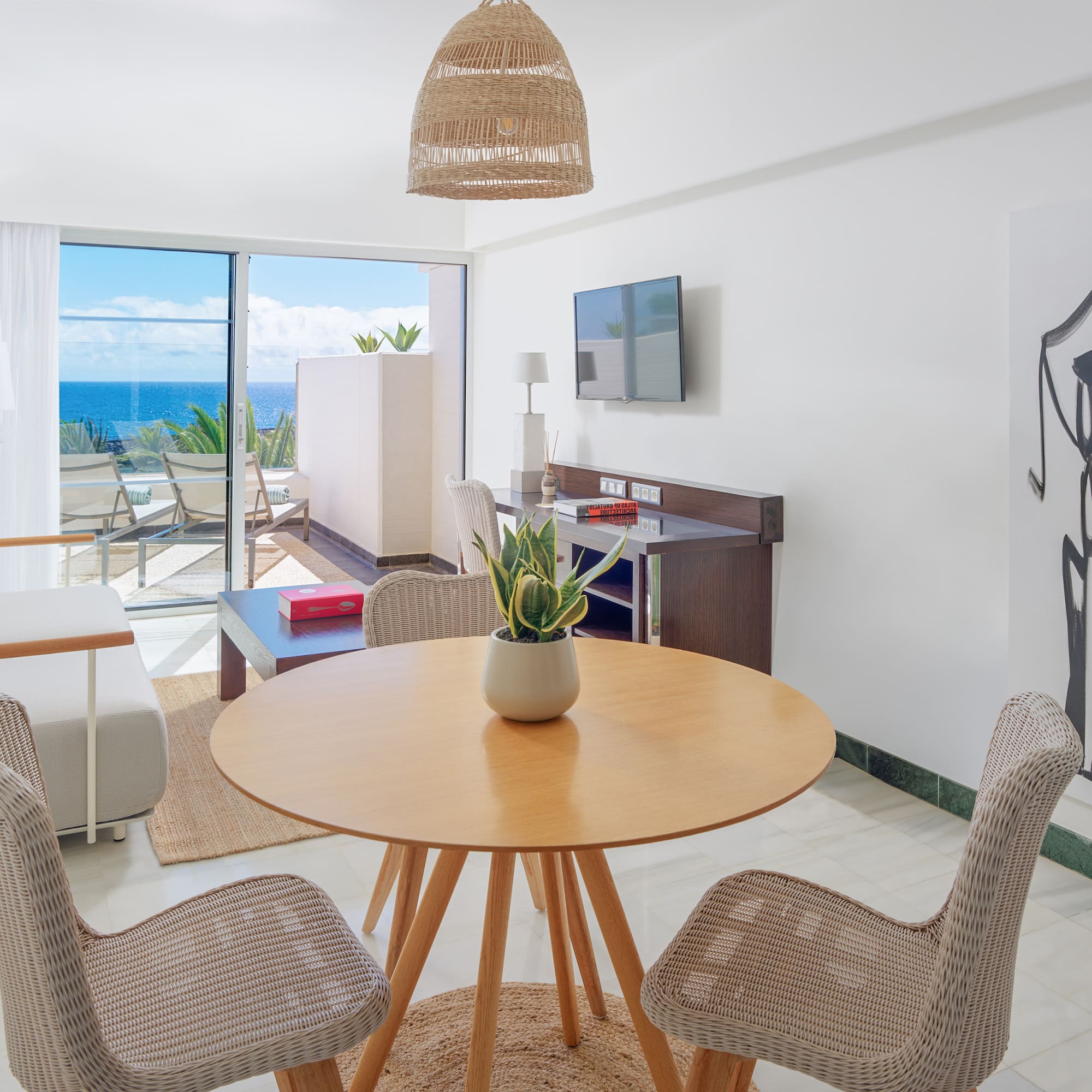 Modern suite living room with ocean view balcony, rattan furniture, and abstract art.