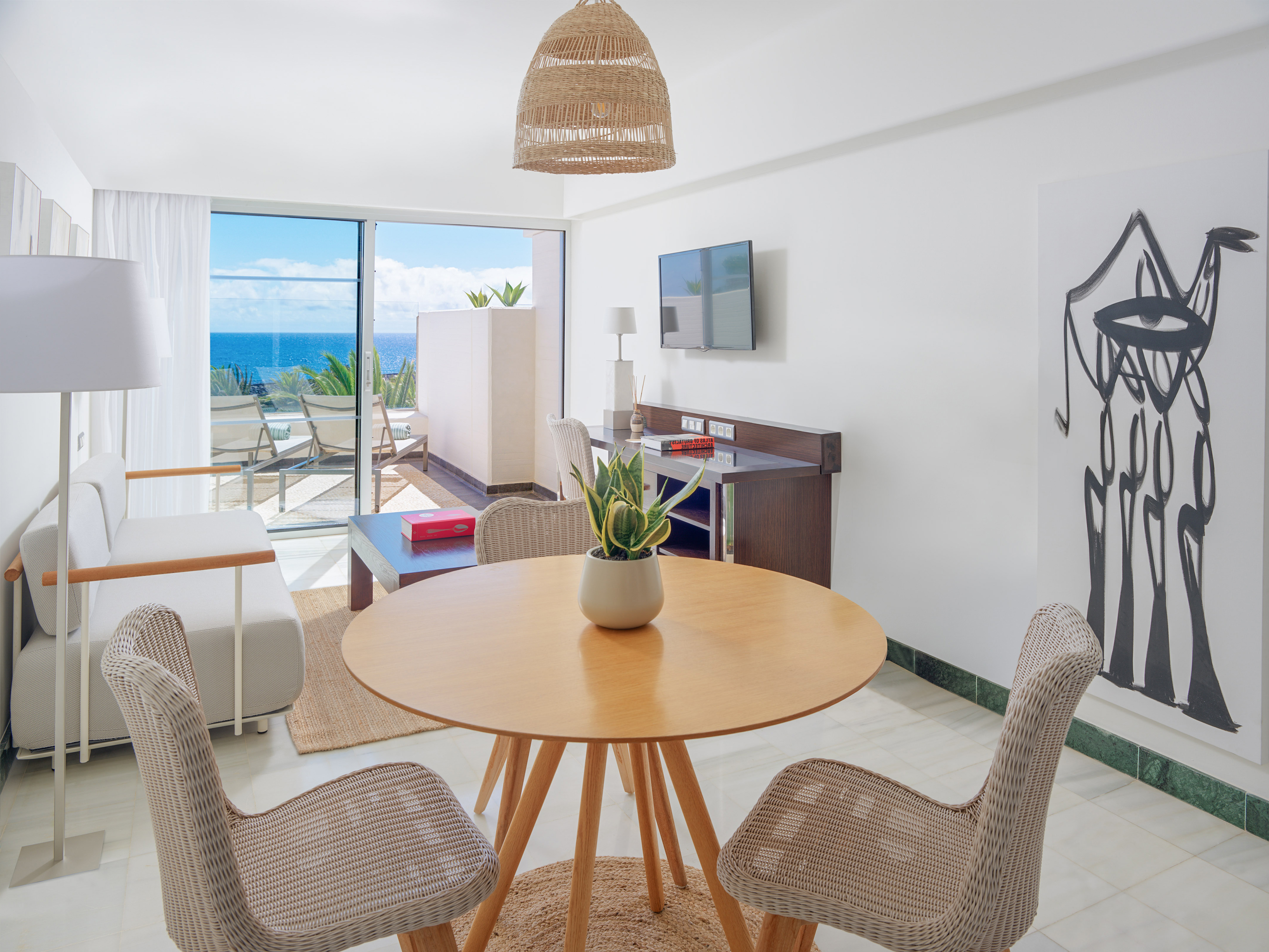 Modern suite living room with ocean view balcony, rattan furniture, and abstract art.