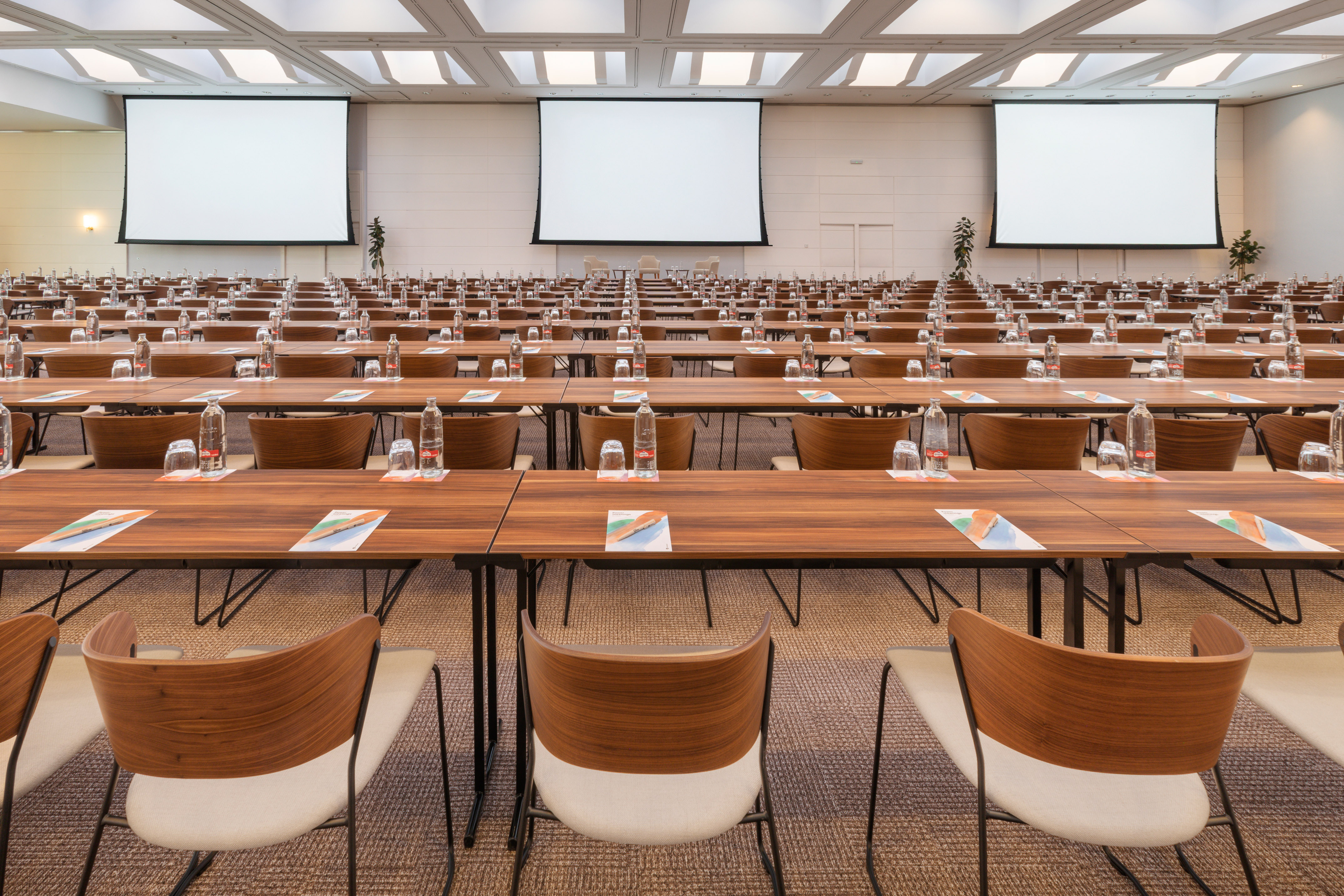 Empty conference room with tables, chairs, and multiple projector screens.