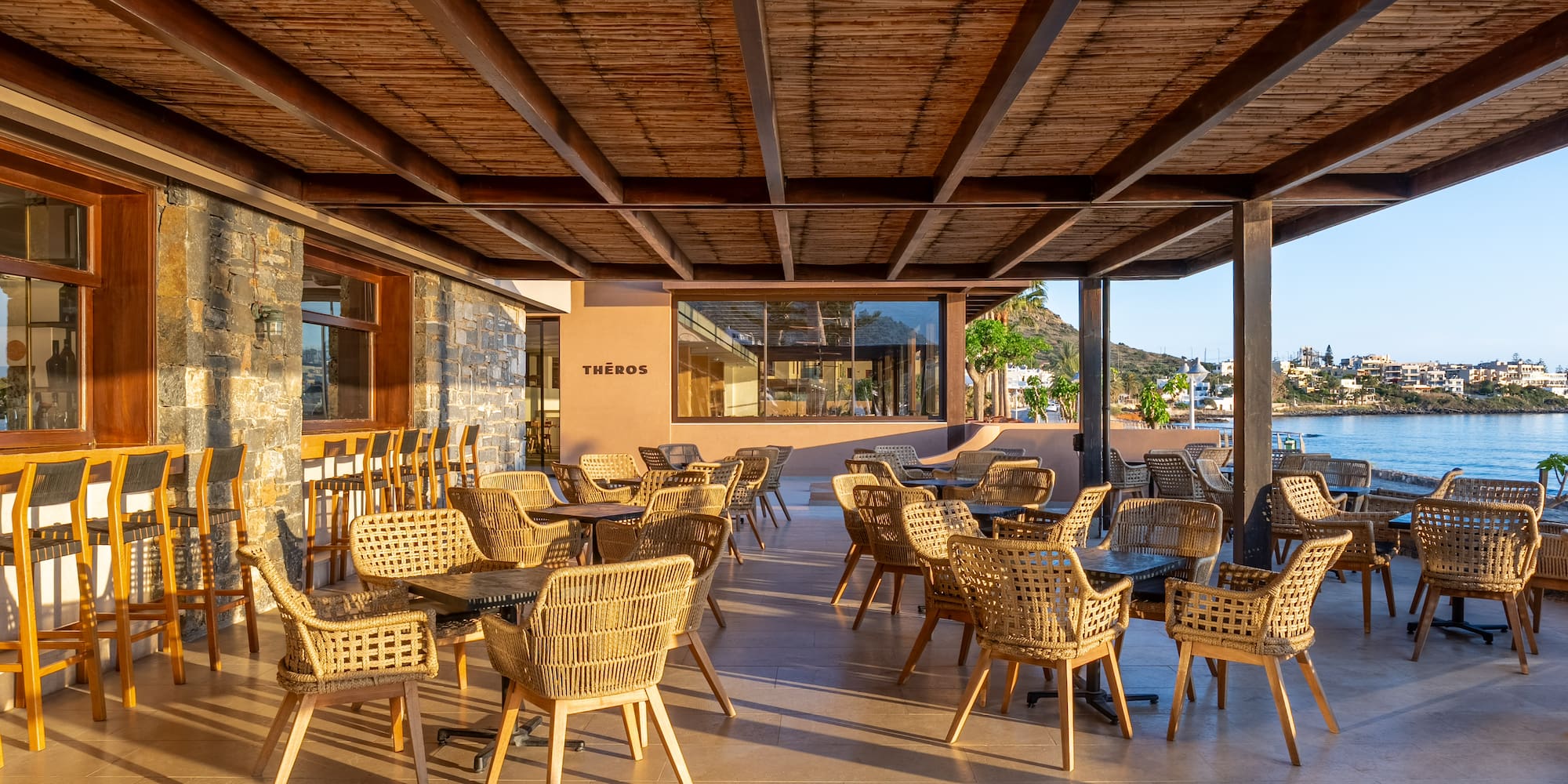 Theros outdoor restaurant patio with wicker seating and sea view.