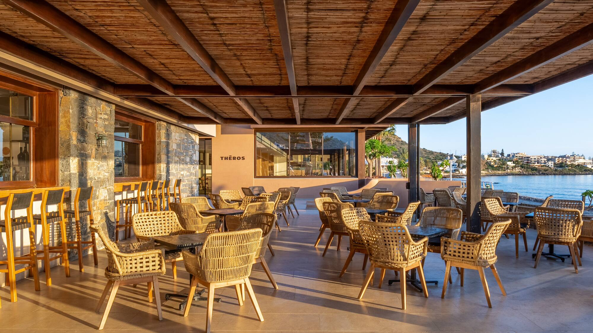Theros outdoor restaurant patio with wicker seating and sea view.