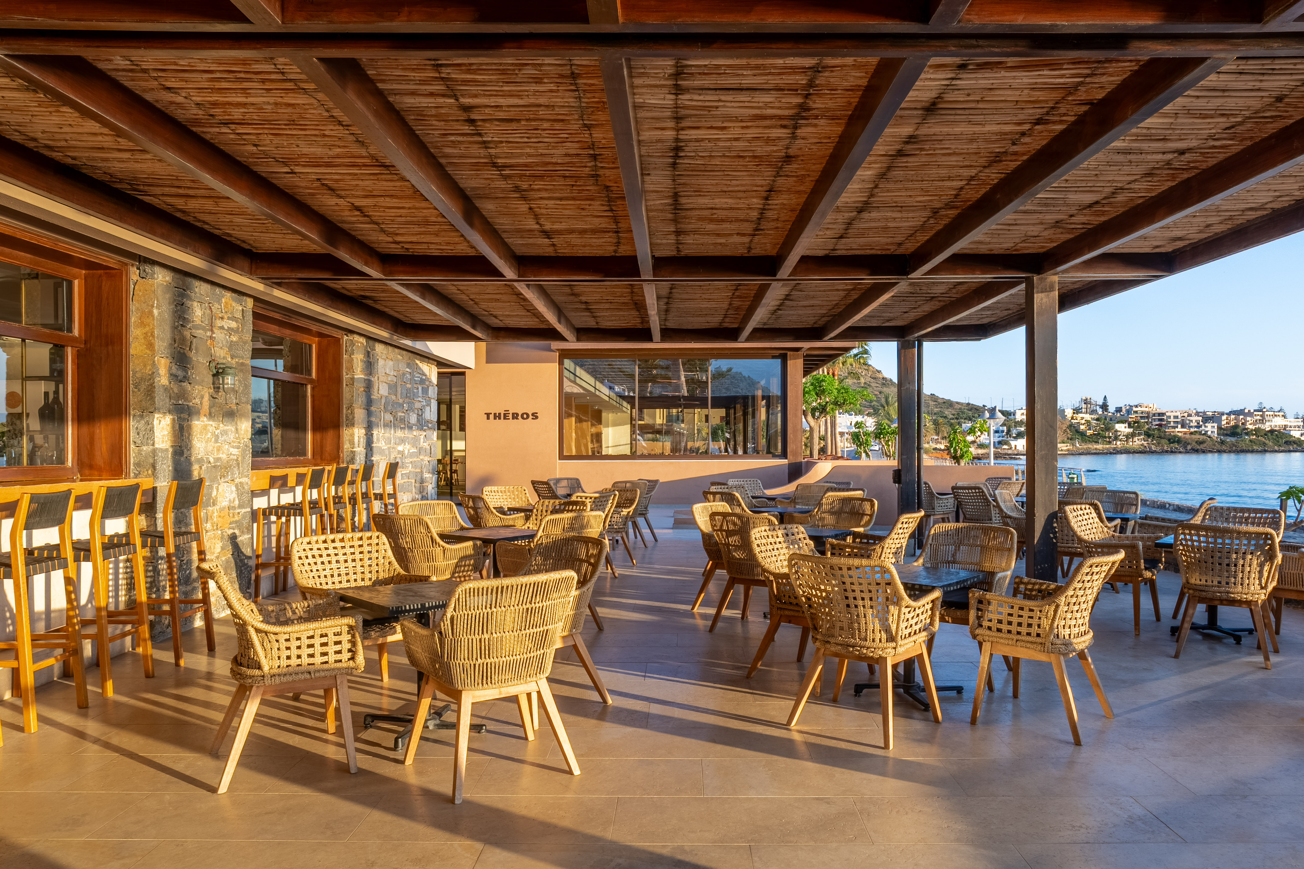 Theros outdoor restaurant patio with wicker seating and sea view.