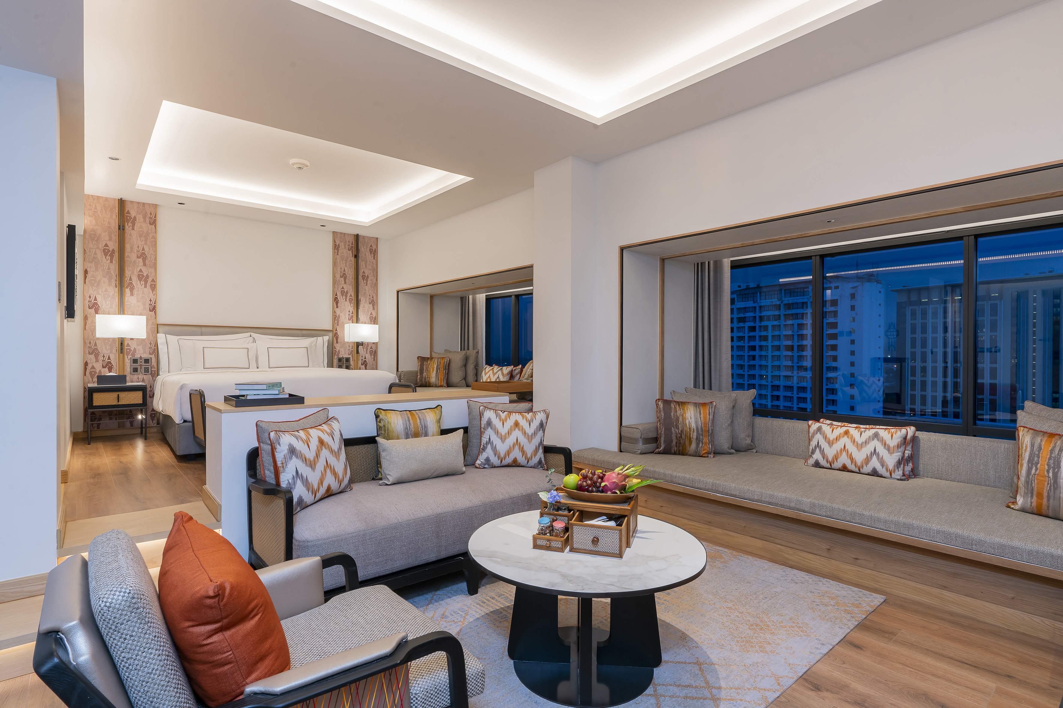 Luxury hotel suite with modern bedroom, living area, and city skyline view.