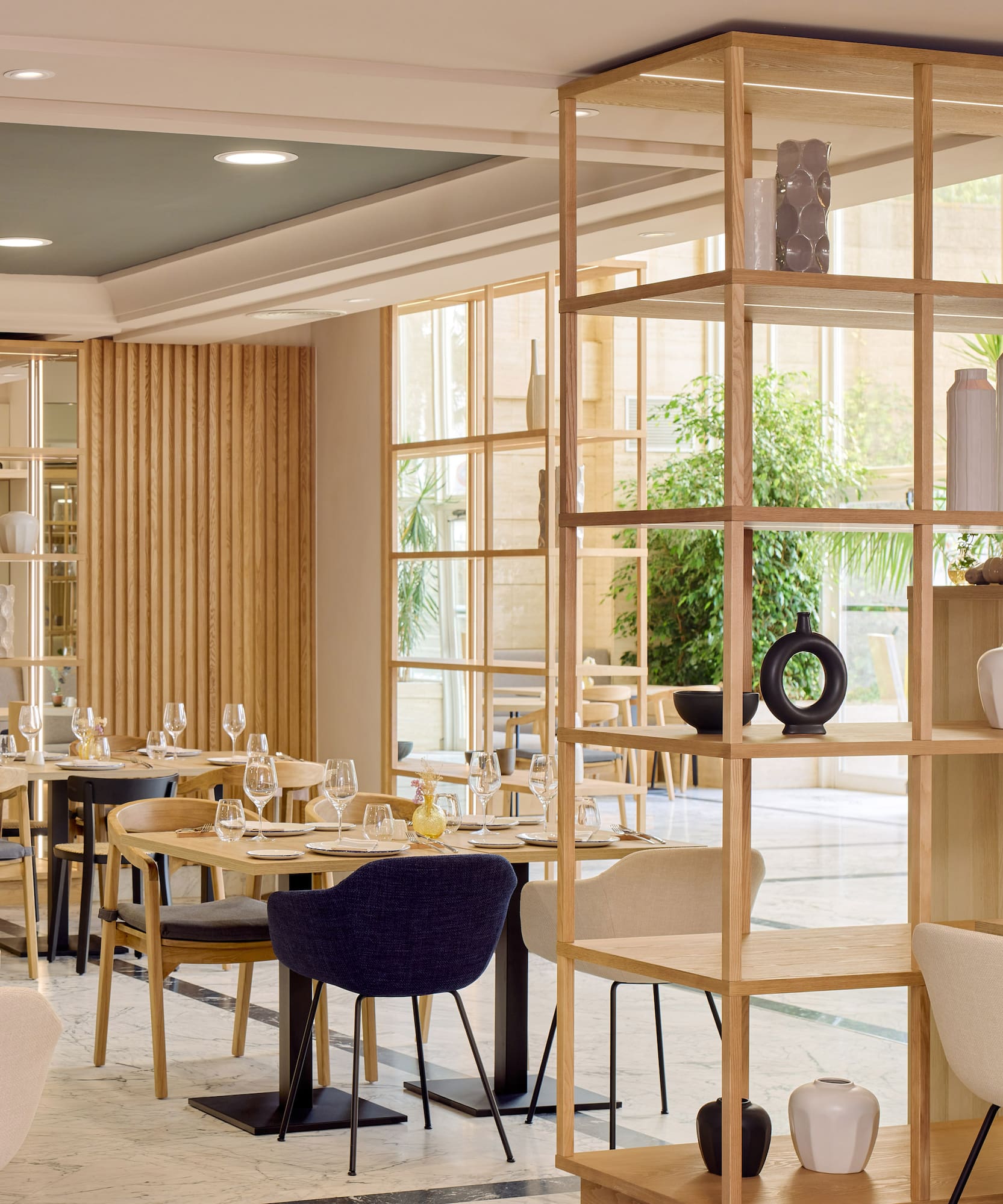 Restaurante moderno con mesas puestas, estanterías de madera y ambiente luminoso.
