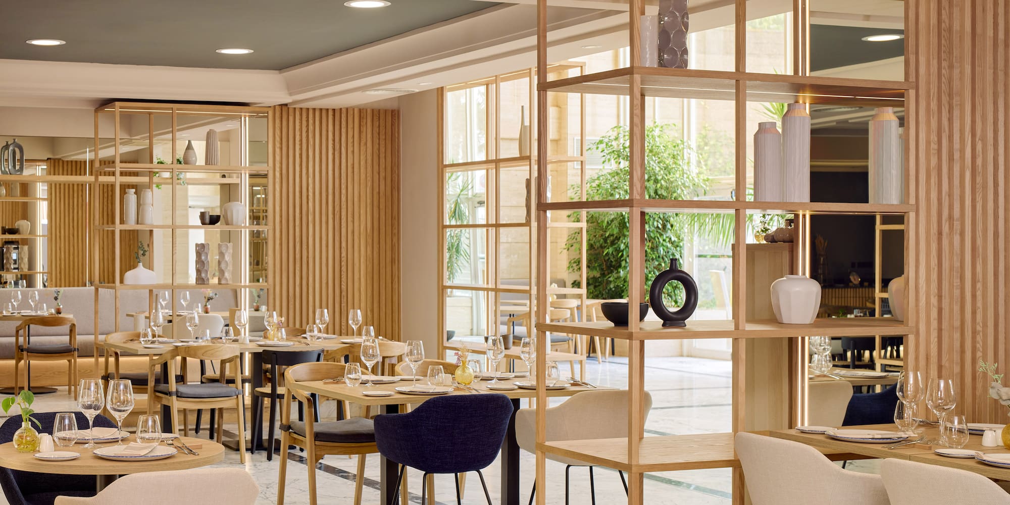 Restaurante moderno con mesas puestas, estanterías de madera y ambiente luminoso.