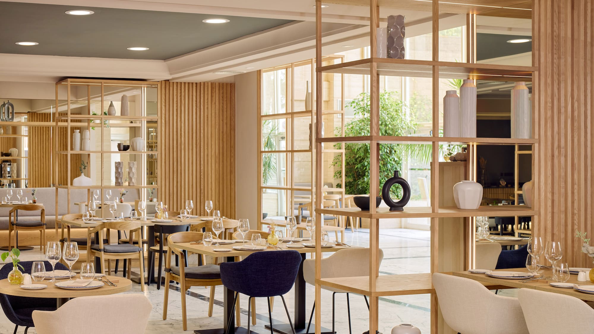Interior de restaurante moderno con mesas de madera, sillas y estanterías divisorias.