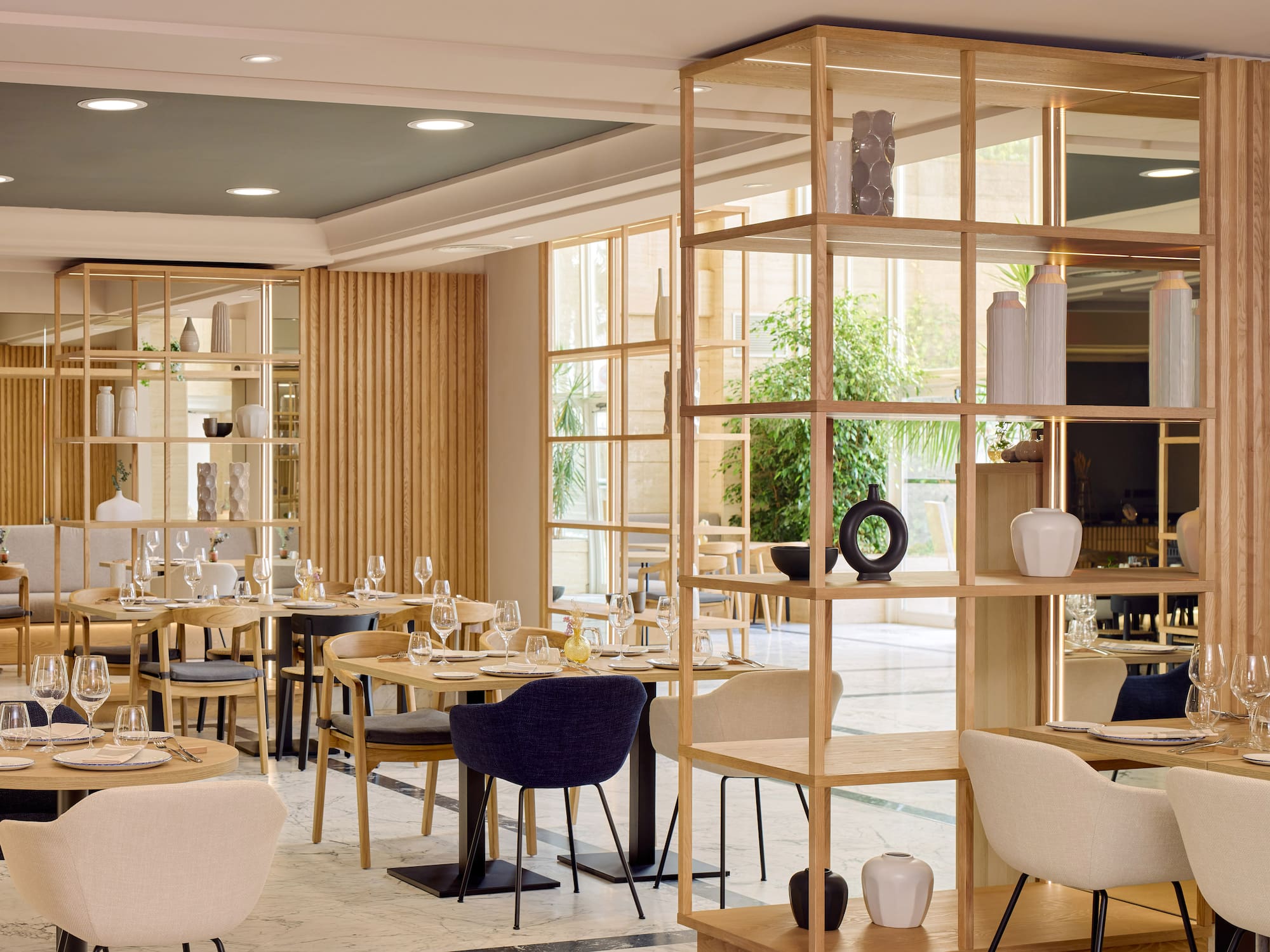 Restaurante moderno, mesas puestas, estanterías de madera y ventanales.