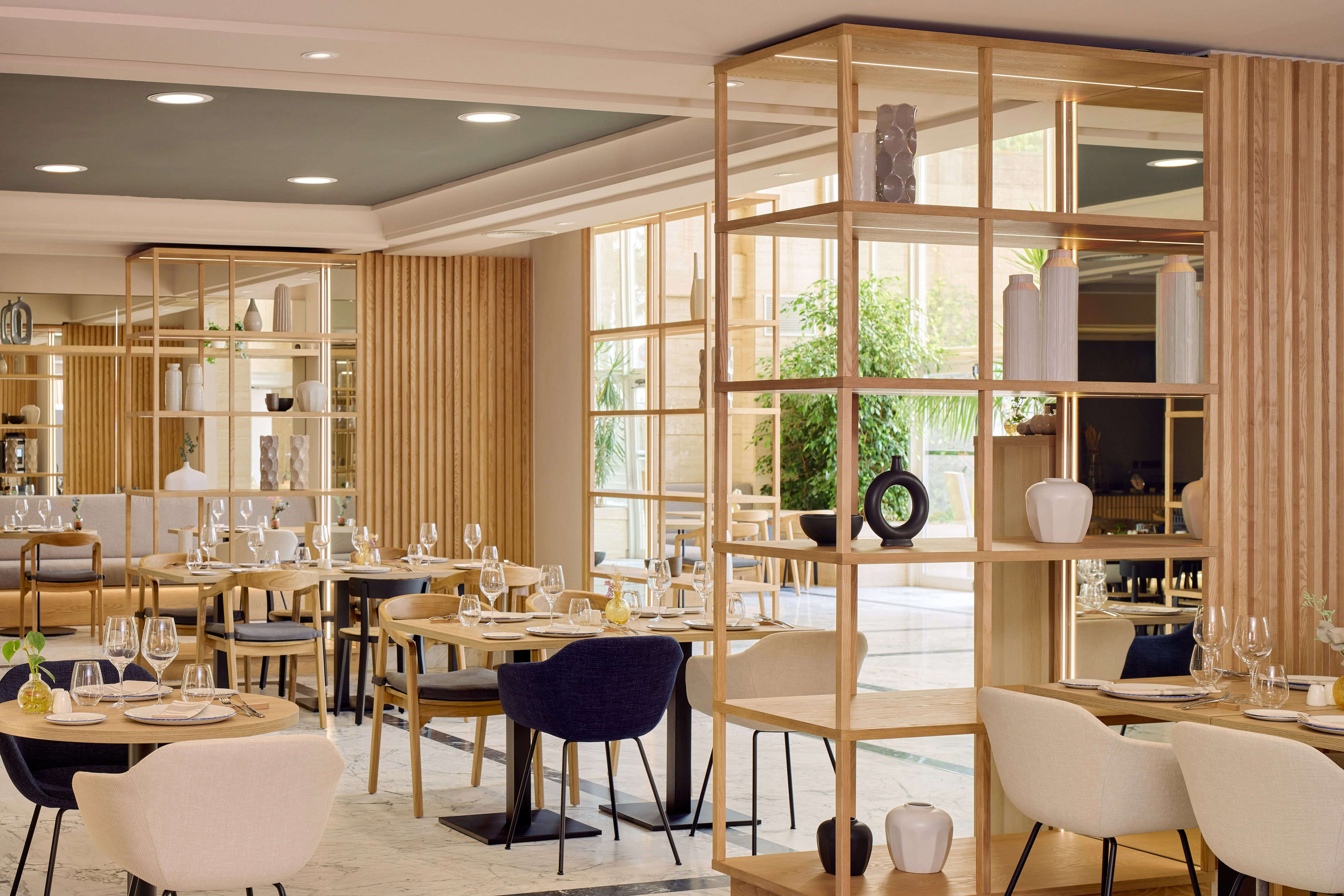 Interior de restaurante moderno con mesas de madera, sillas y estanterías divisorias.
