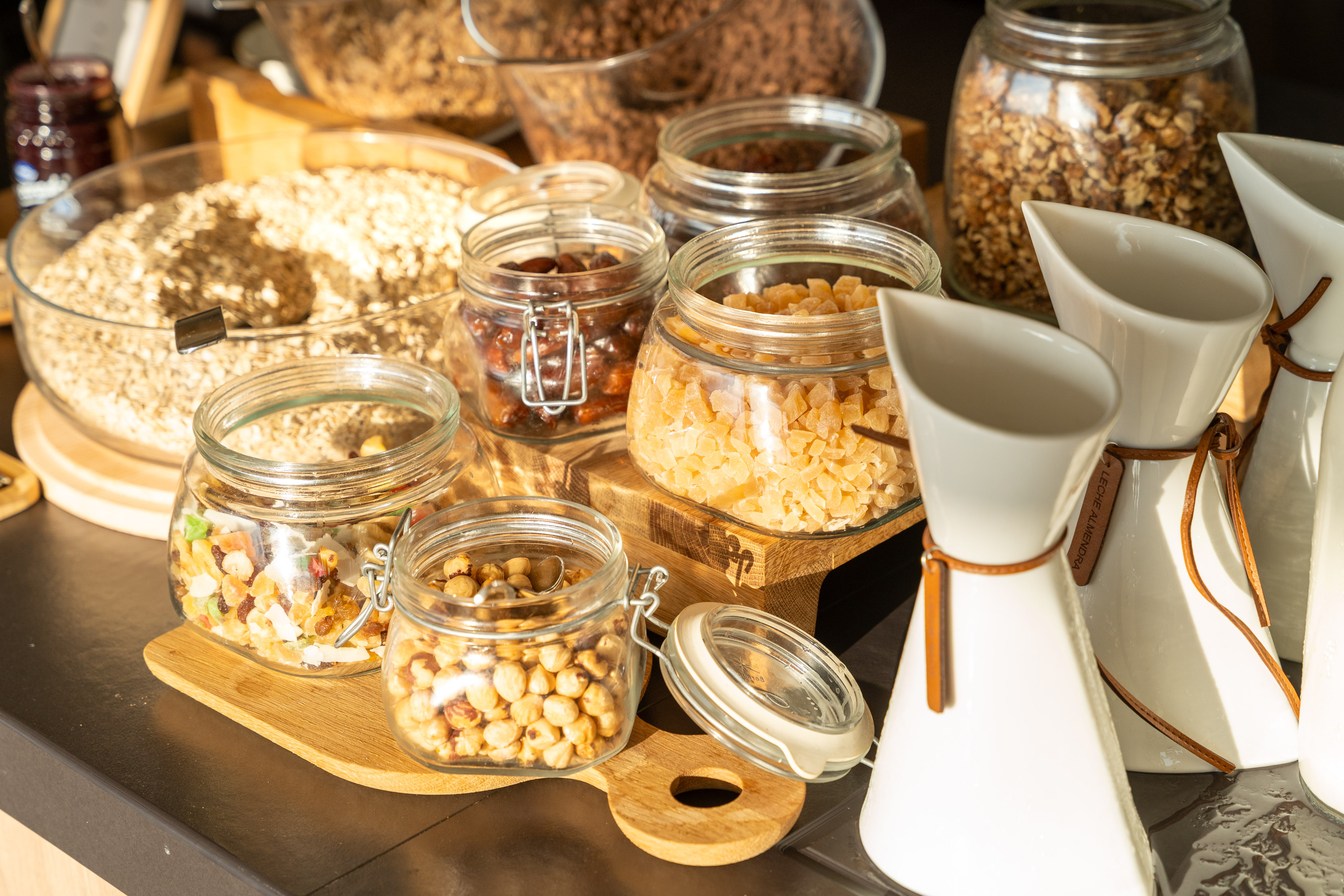 Breakfast buffet: oats, granola, nuts, dried fruit in jars, almond milk carafes.