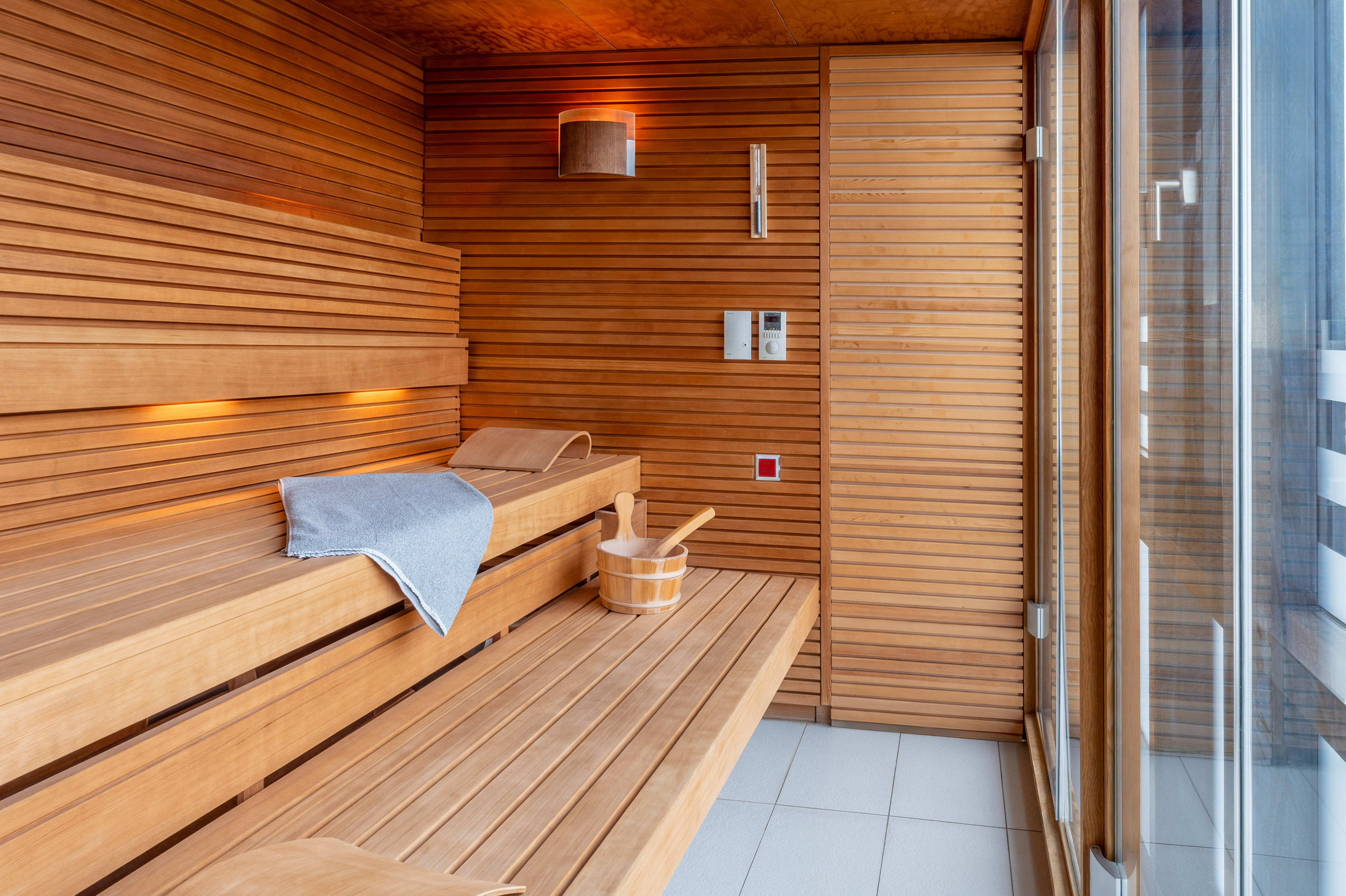 Modern wooden sauna interior with slatted benches, towel, and bucket.