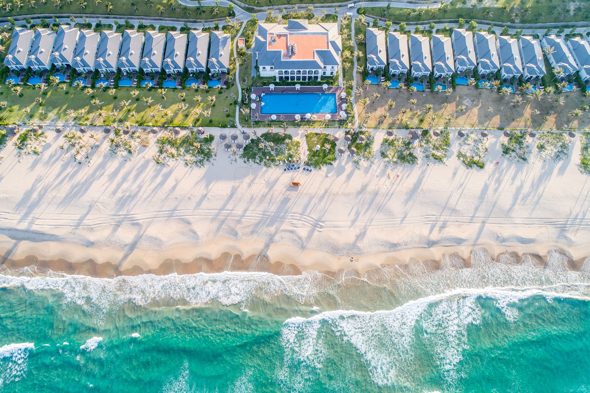 Aerial beach resort with villas, pools, sandy beach, and turquoise ocean.