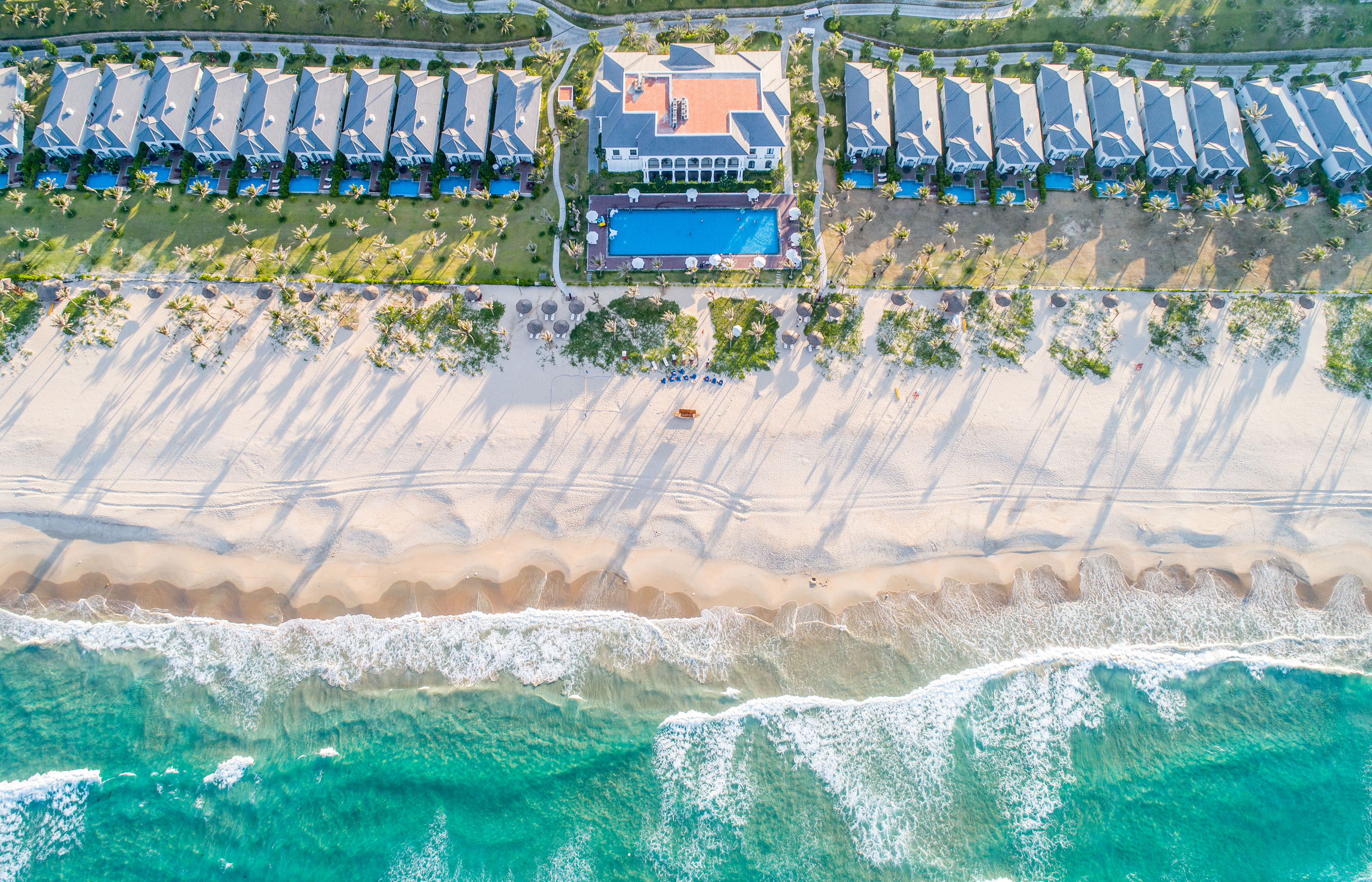 Aerial beach resort with villas, pools, sandy beach, and turquoise ocean.