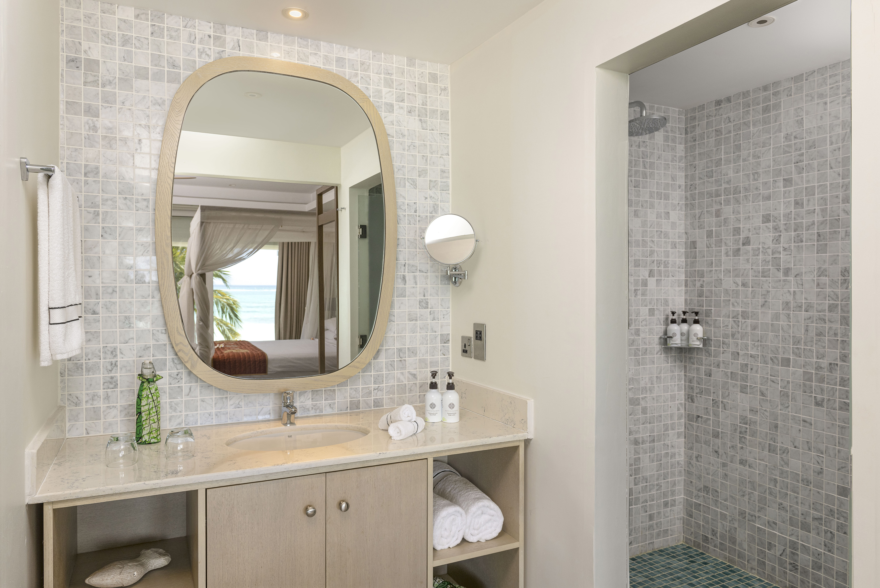 Hotel bathroom vanity with marble tile shower and ocean view reflection.