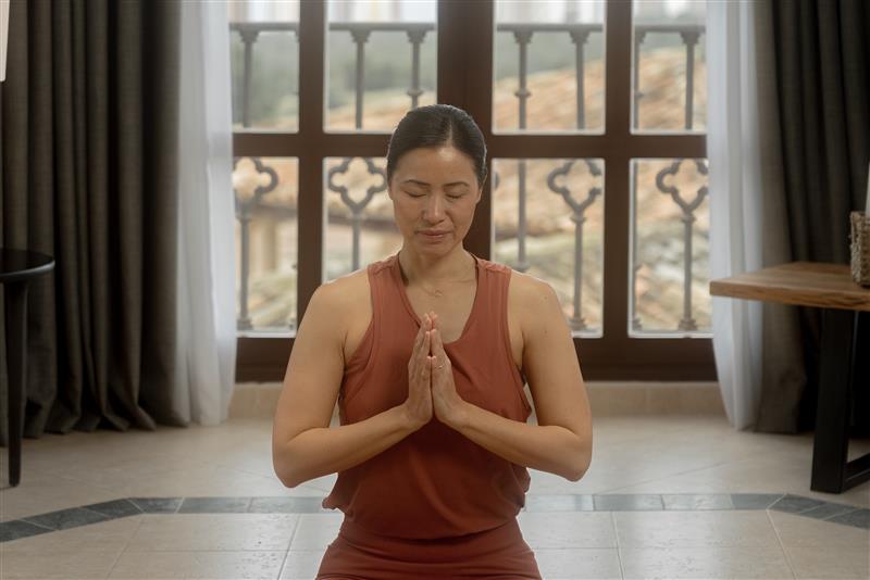 Woman meditating in prayer pose indoors by a decorative window.