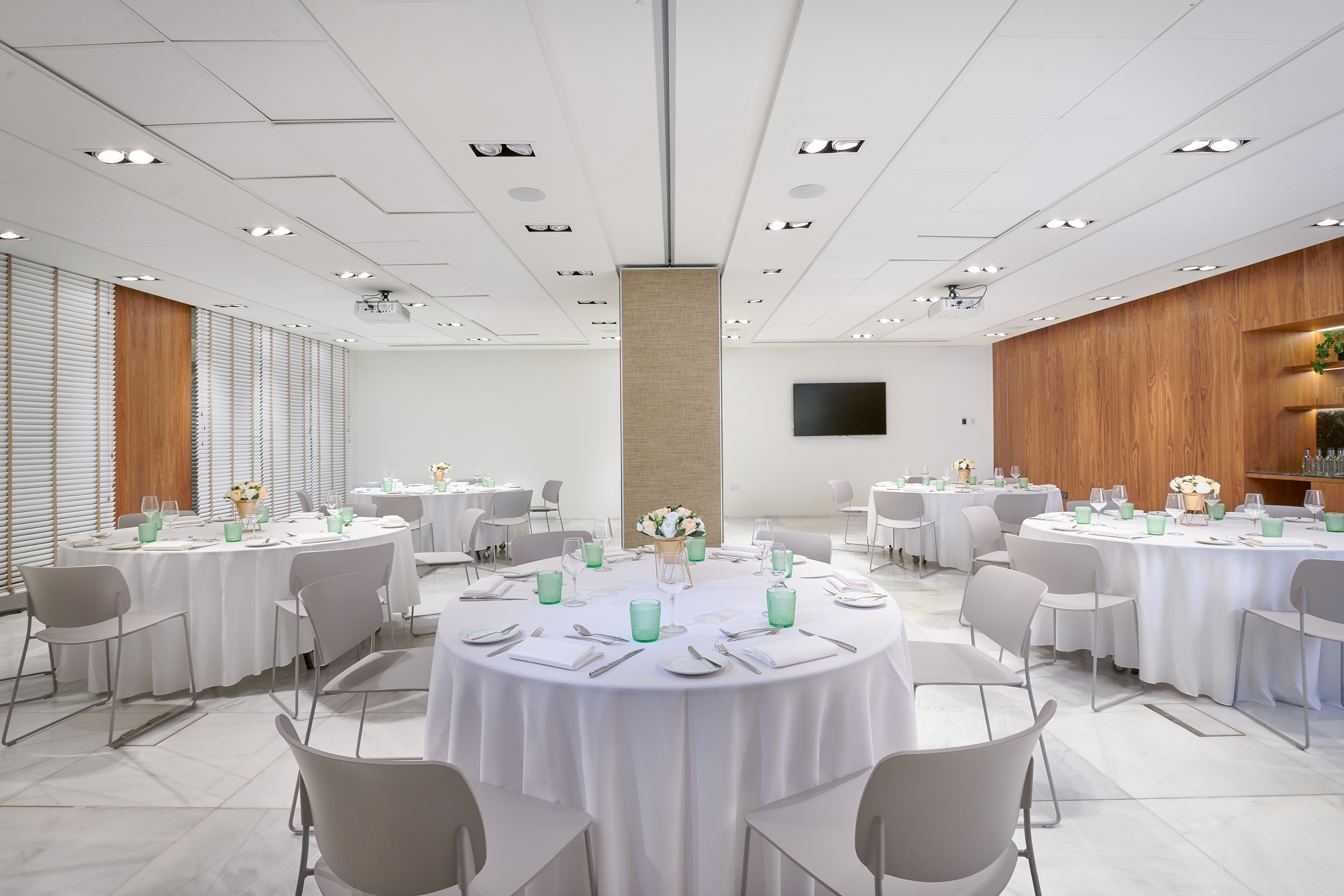 Modern event room with round tables, white linens, grey chairs, and projector.
