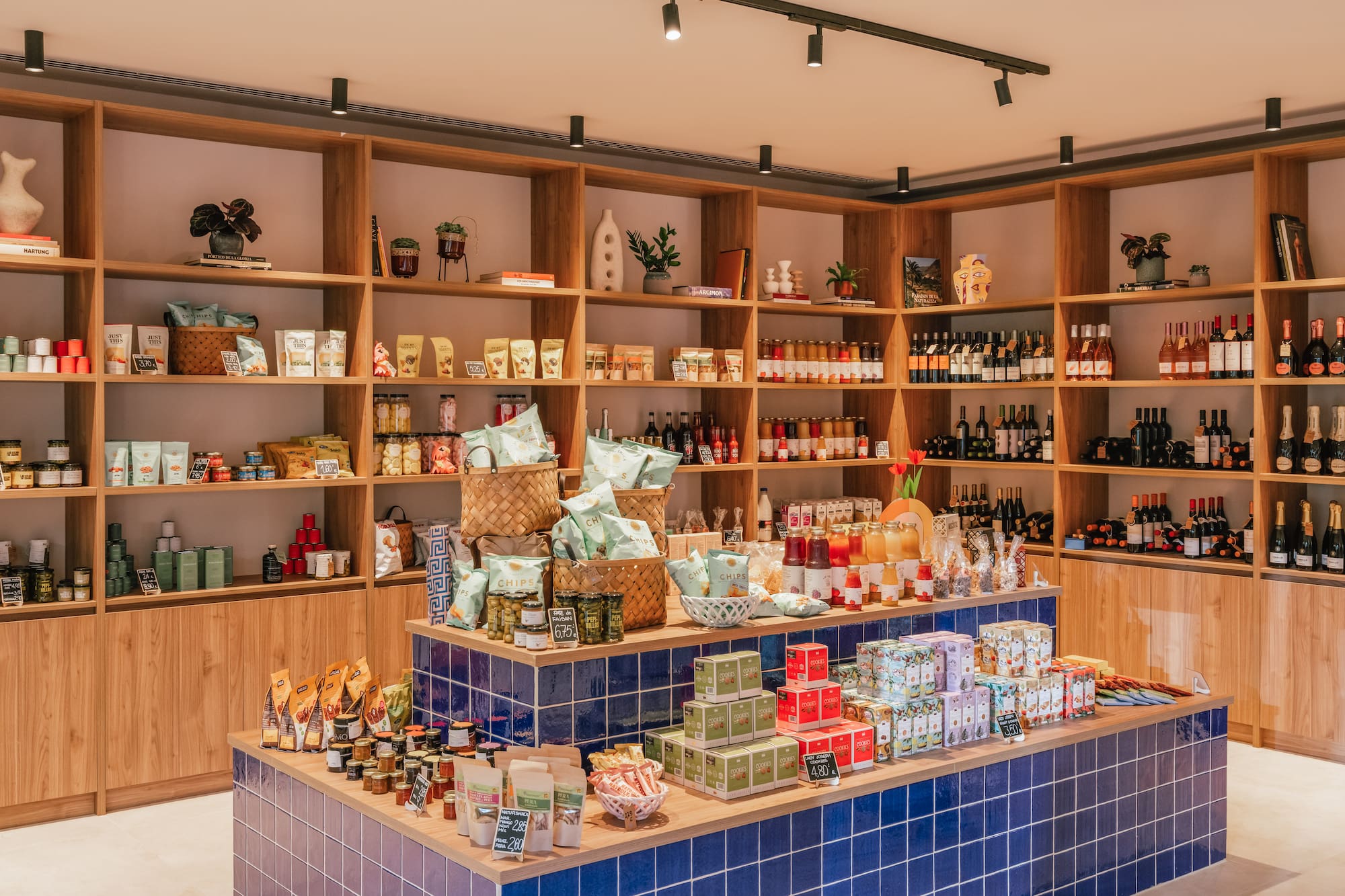 Modern gourmet grocery shop with wooden shelves, blue tiled counter, and products.