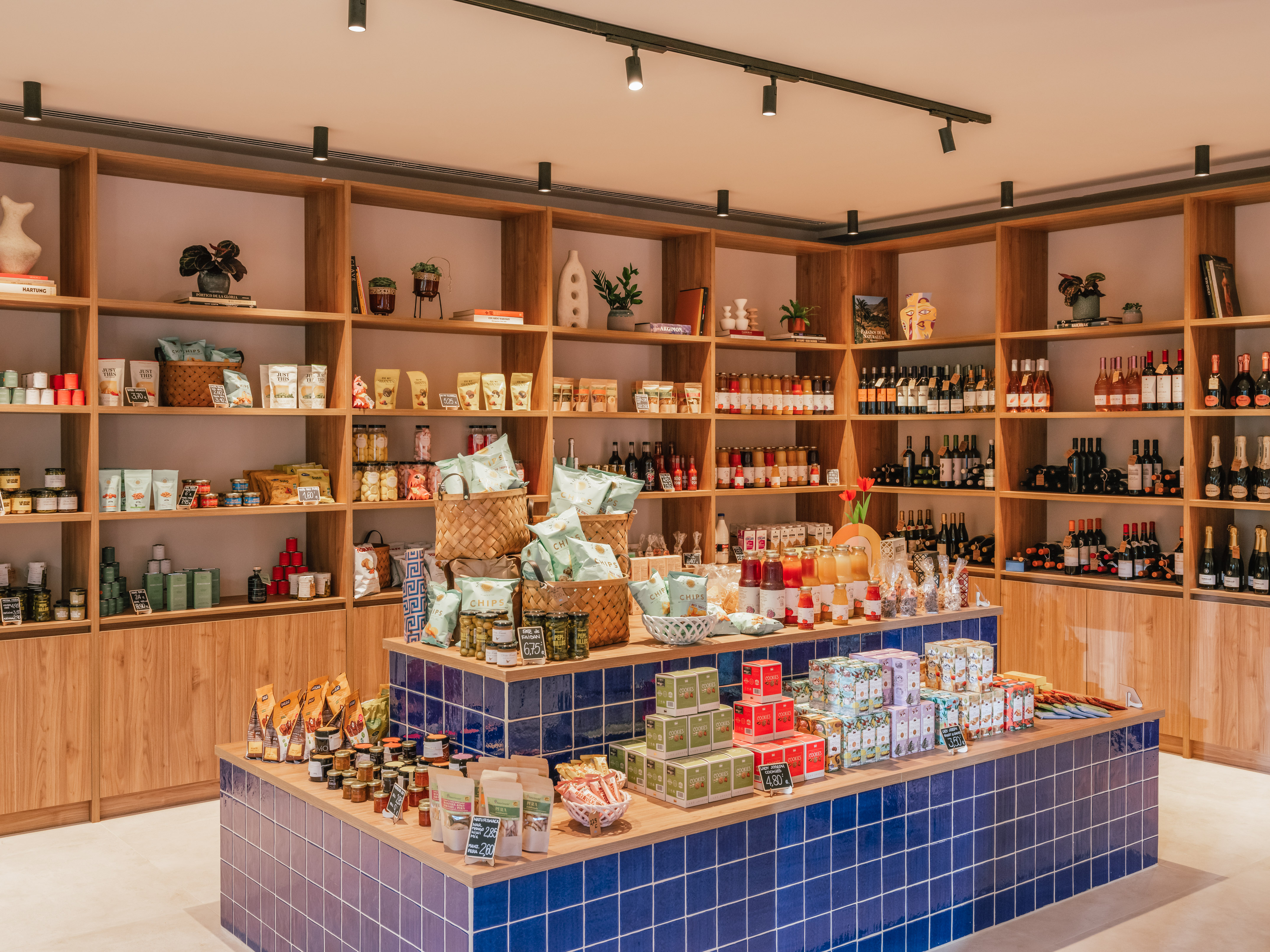 Modern gourmet grocery shop with wooden shelves, blue tiled counter, and products.