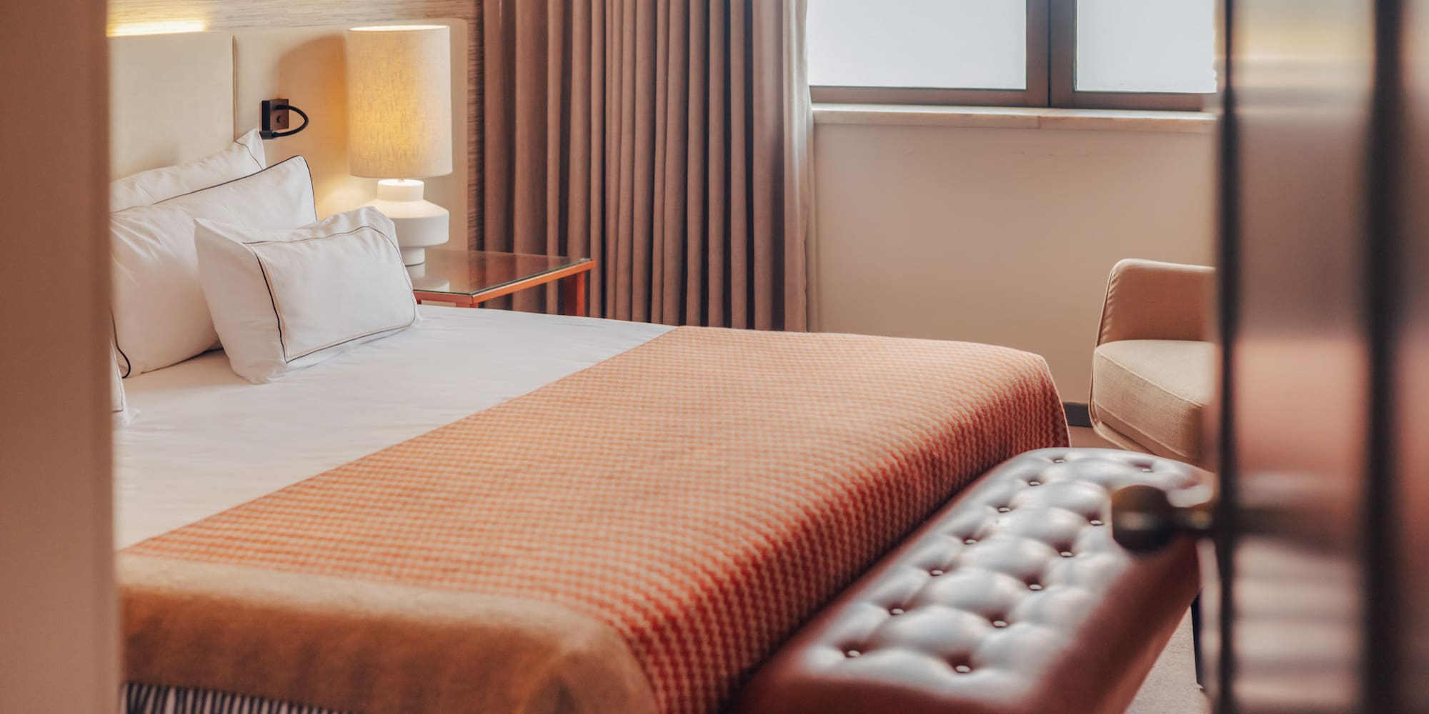 Hotel bedroom with a bed, orange patterned throw, and tufted leather bench.
