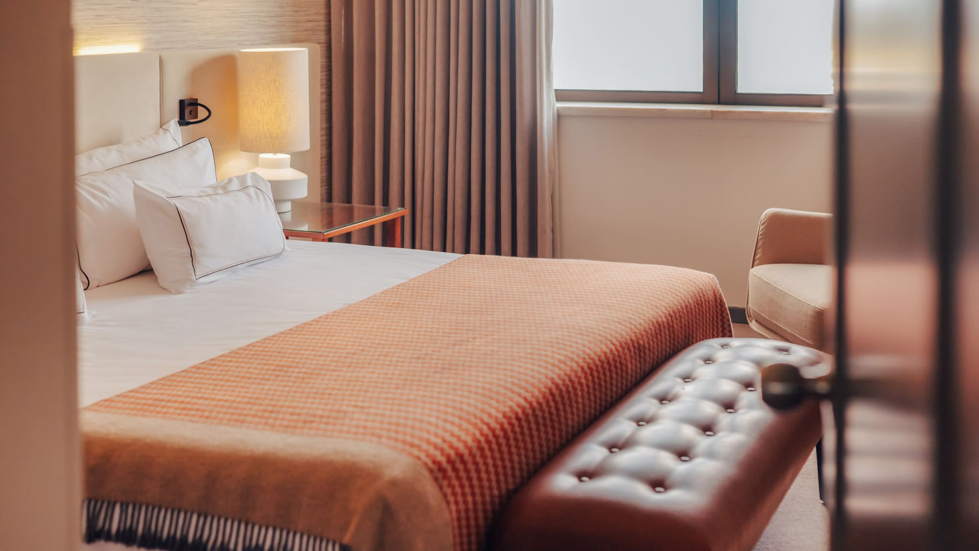 Hotel bedroom with a bed, orange patterned throw, and tufted leather bench.