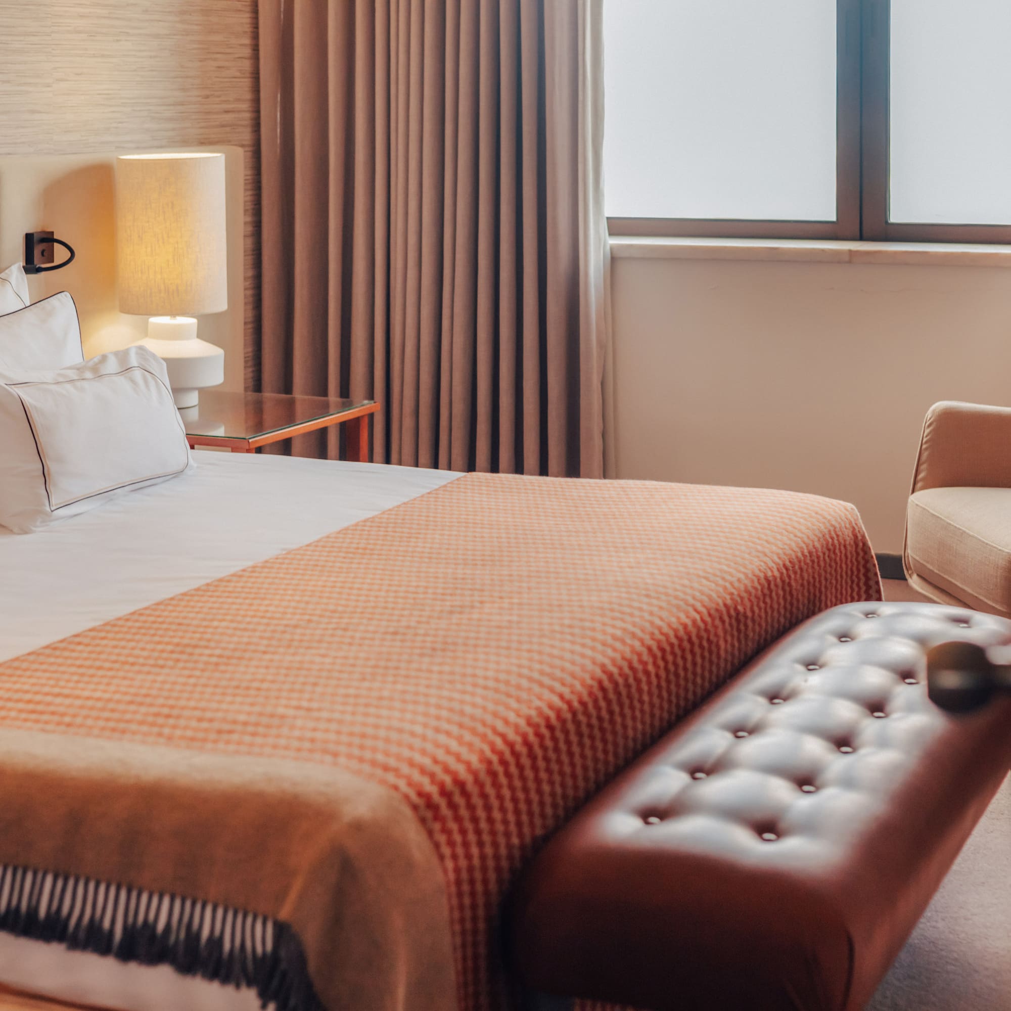 Hotel bedroom with a bed, orange patterned throw, and tufted leather bench.
