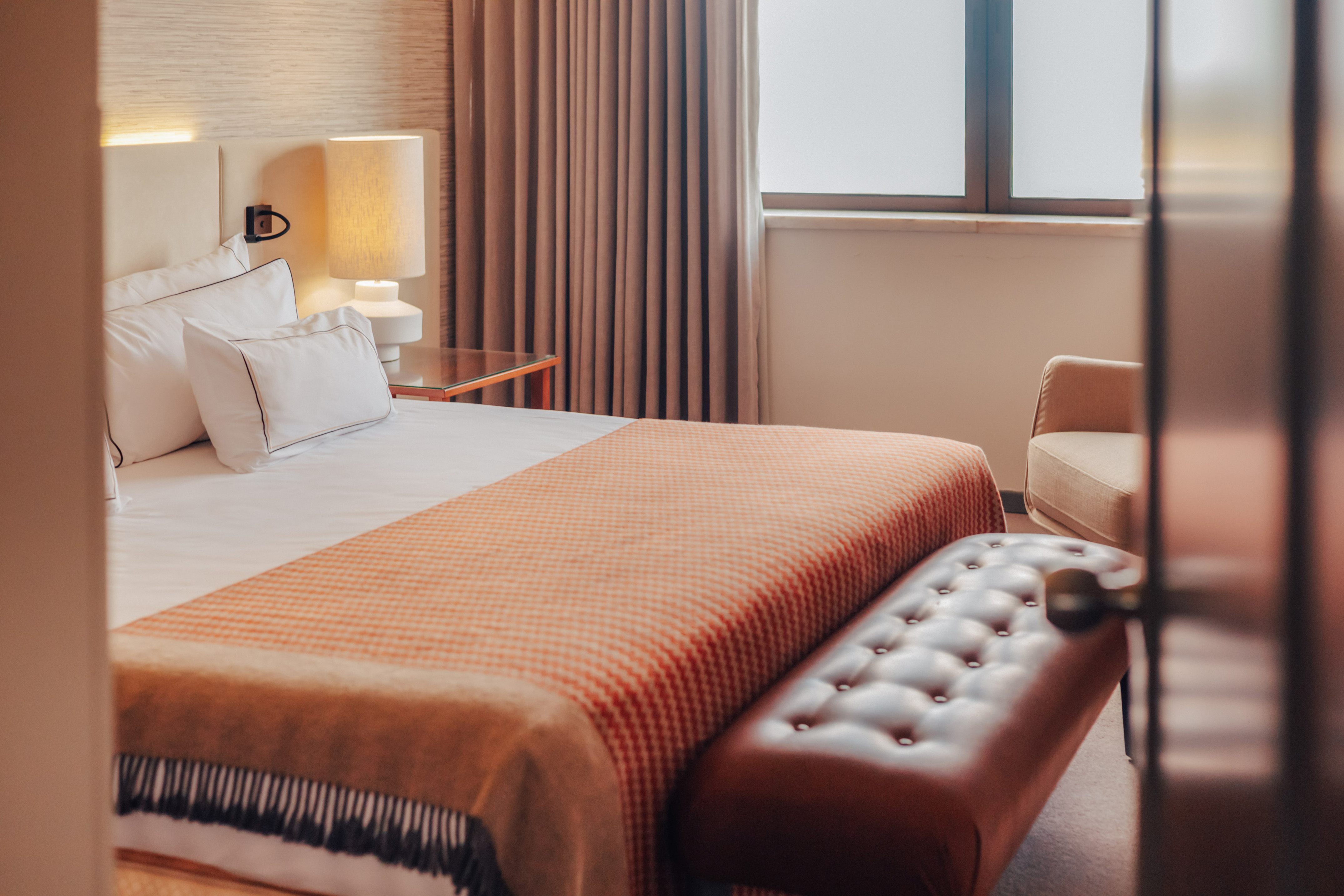 Hotel bedroom with a bed, orange patterned throw, and tufted leather bench.