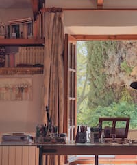 a room with a window open to a table and bookshelf