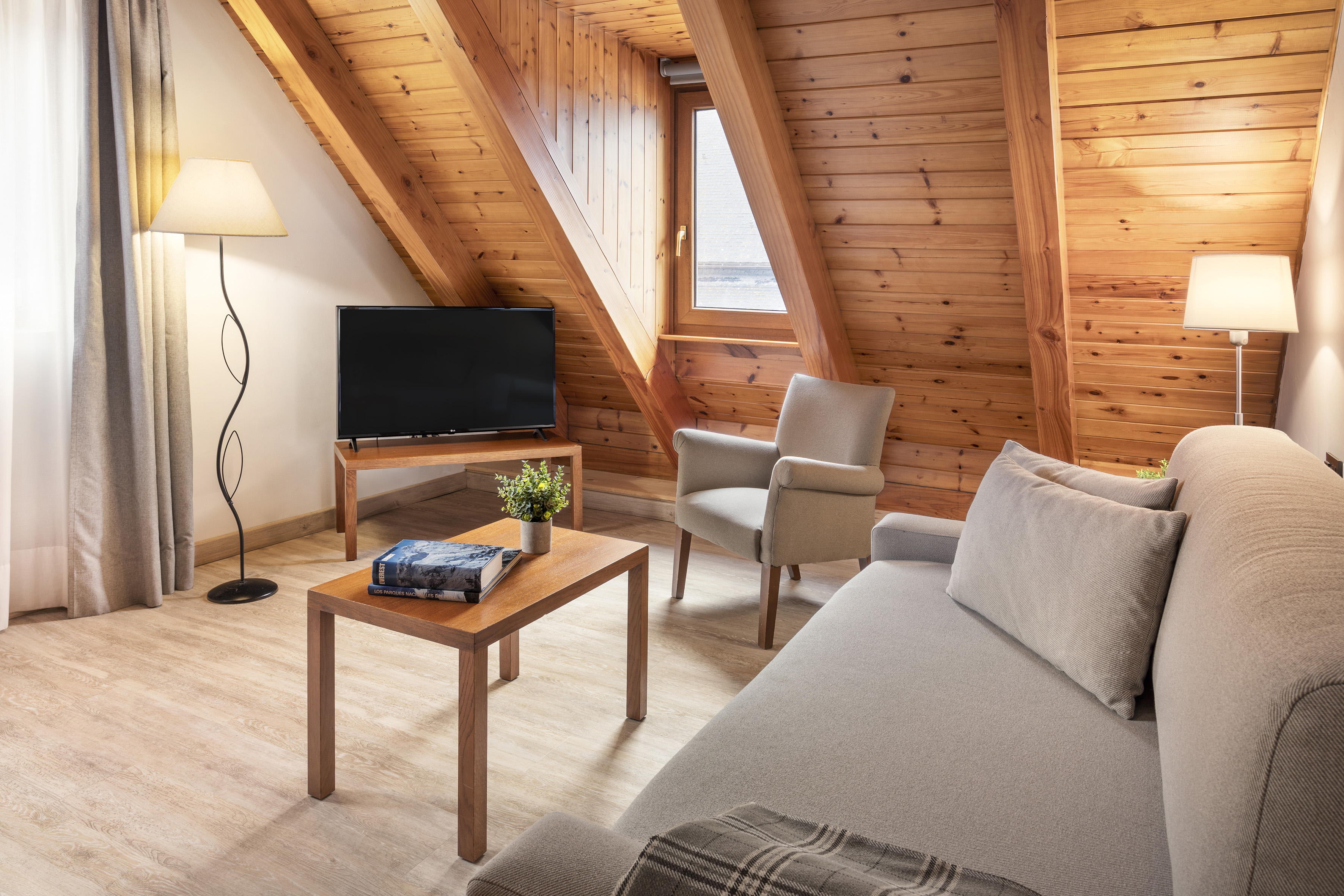 Cozy loft living room with wood paneling, light sofa, armchair, and TV.