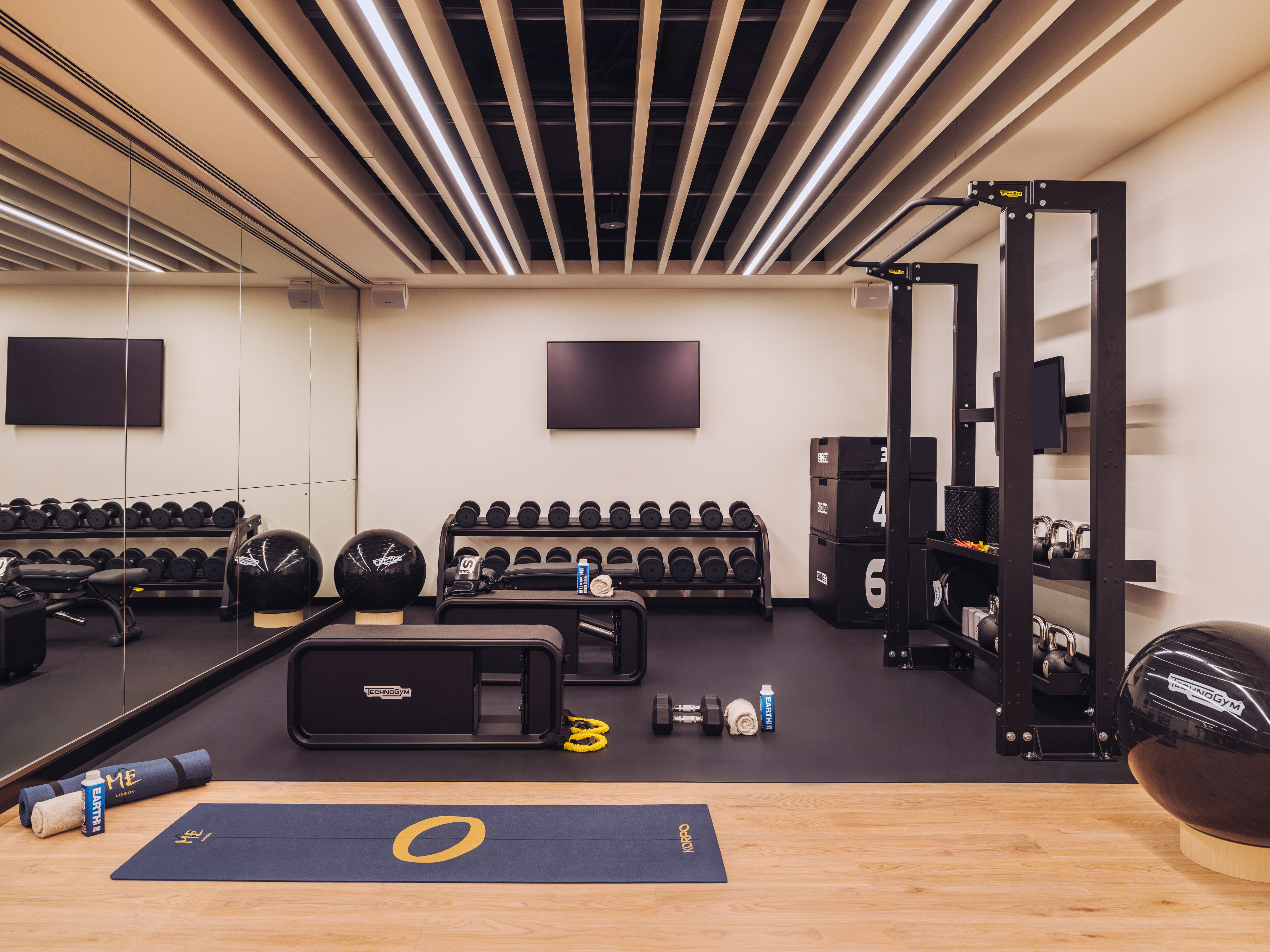 Modern gym with Technogym fitness equipment, dumbbells, kettlebells, and yoga mats.