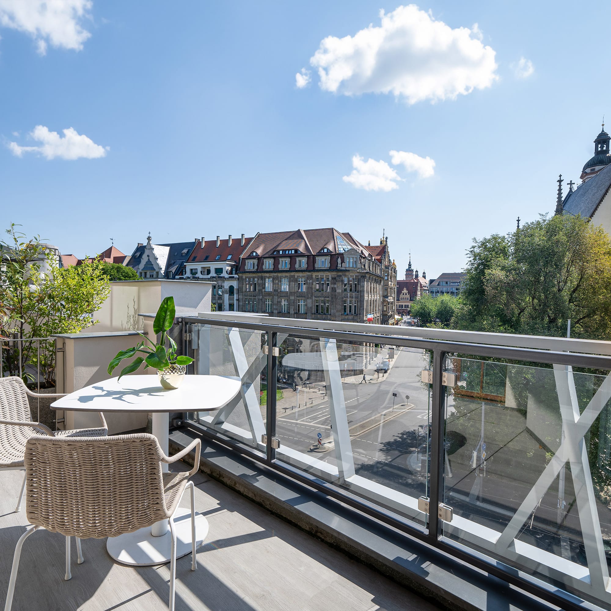 Rooftop balcony with glass railing, outdoor seating, and Leipzig city view with church.