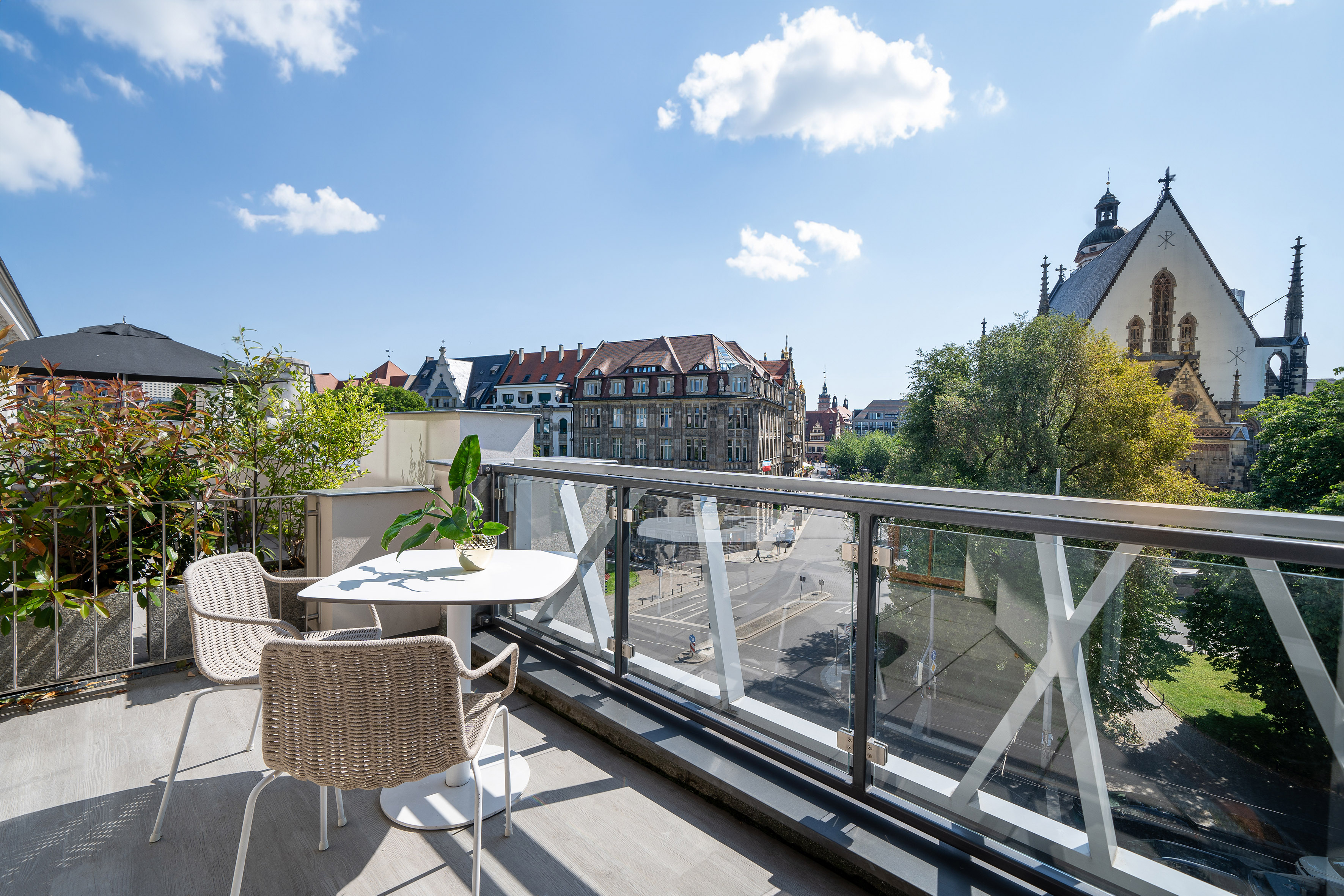 Rooftop balcony with glass railing, outdoor seating, and Leipzig city view with church.