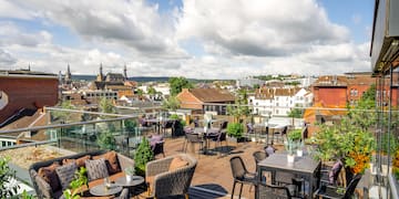 a rooftop patio with chairs and tables and a city in the background