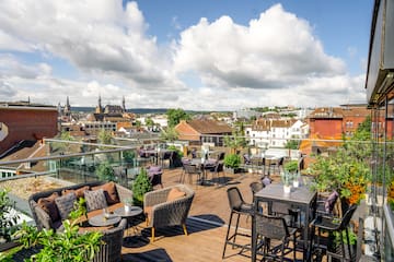 a rooftop patio with chairs and tables and a city in the background