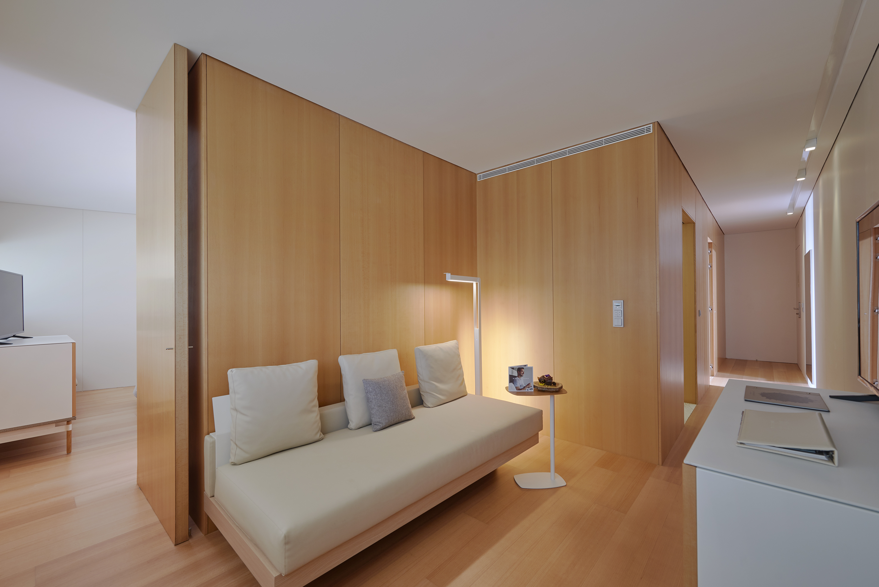 Modern minimalist room: wood paneling, beige daybed, sleek lamp.