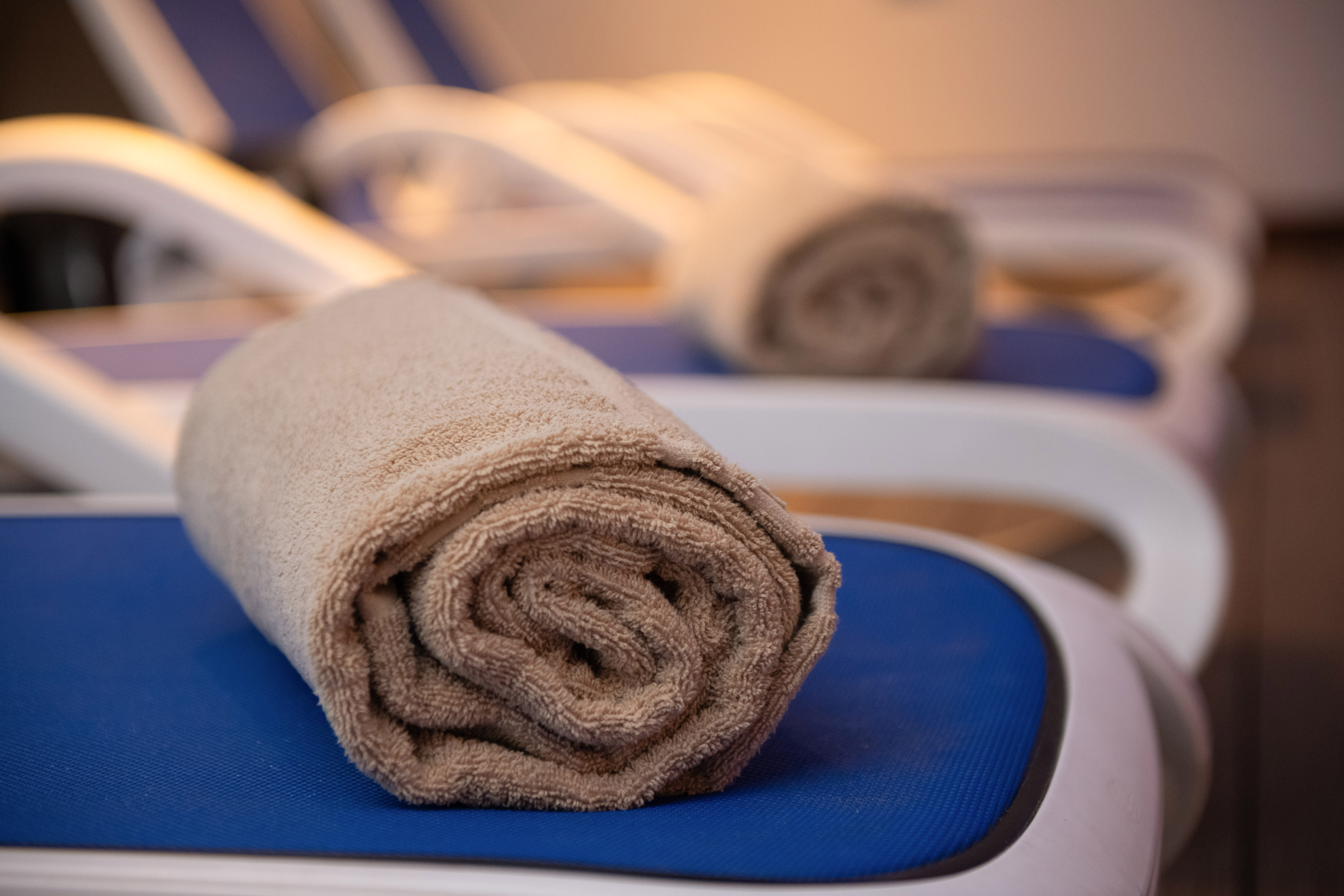Rolled beige towel on a blue lounge chair, ready for spa or poolside relaxation.