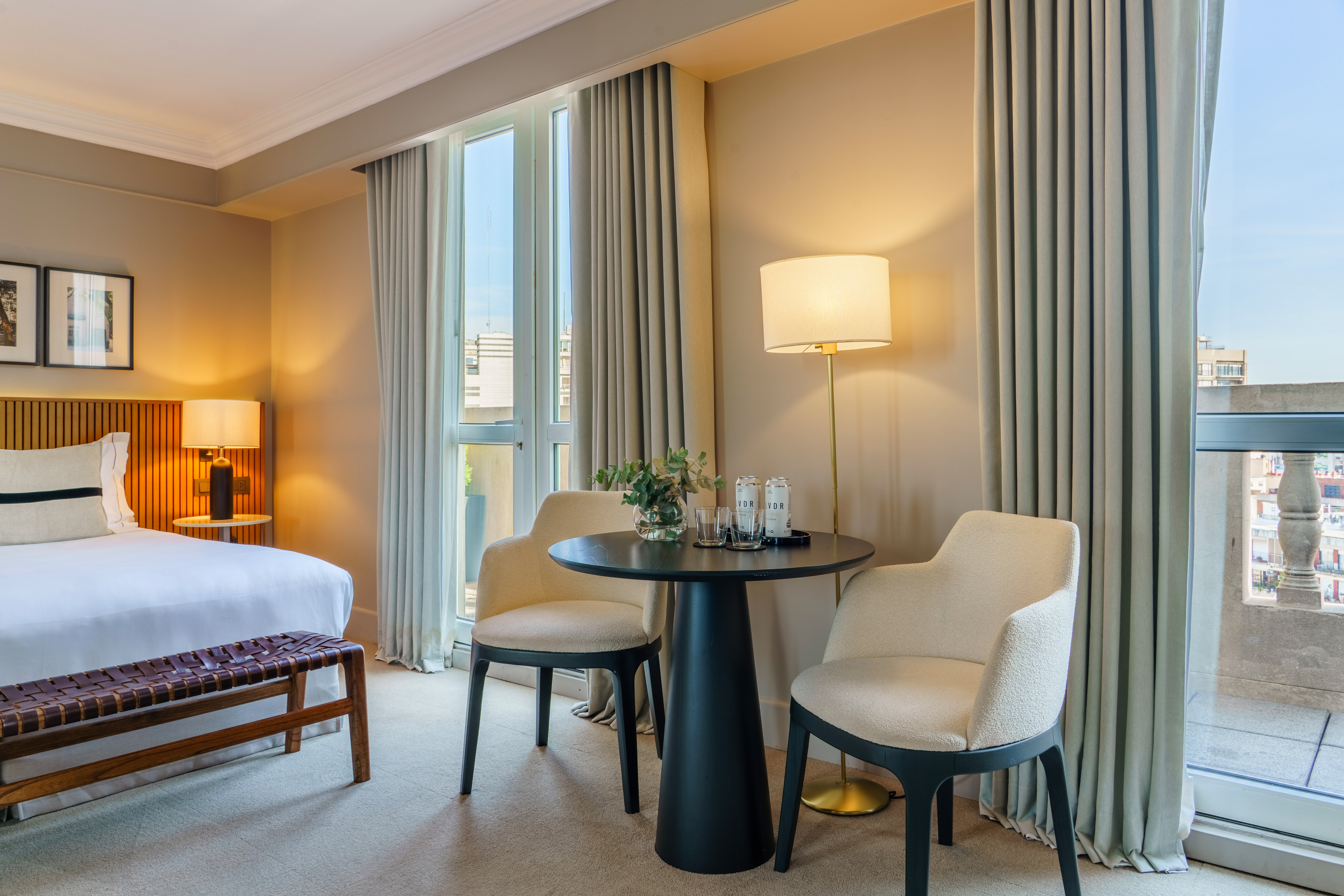 Modern hotel room with bed, sitting area, large windows, and balcony.