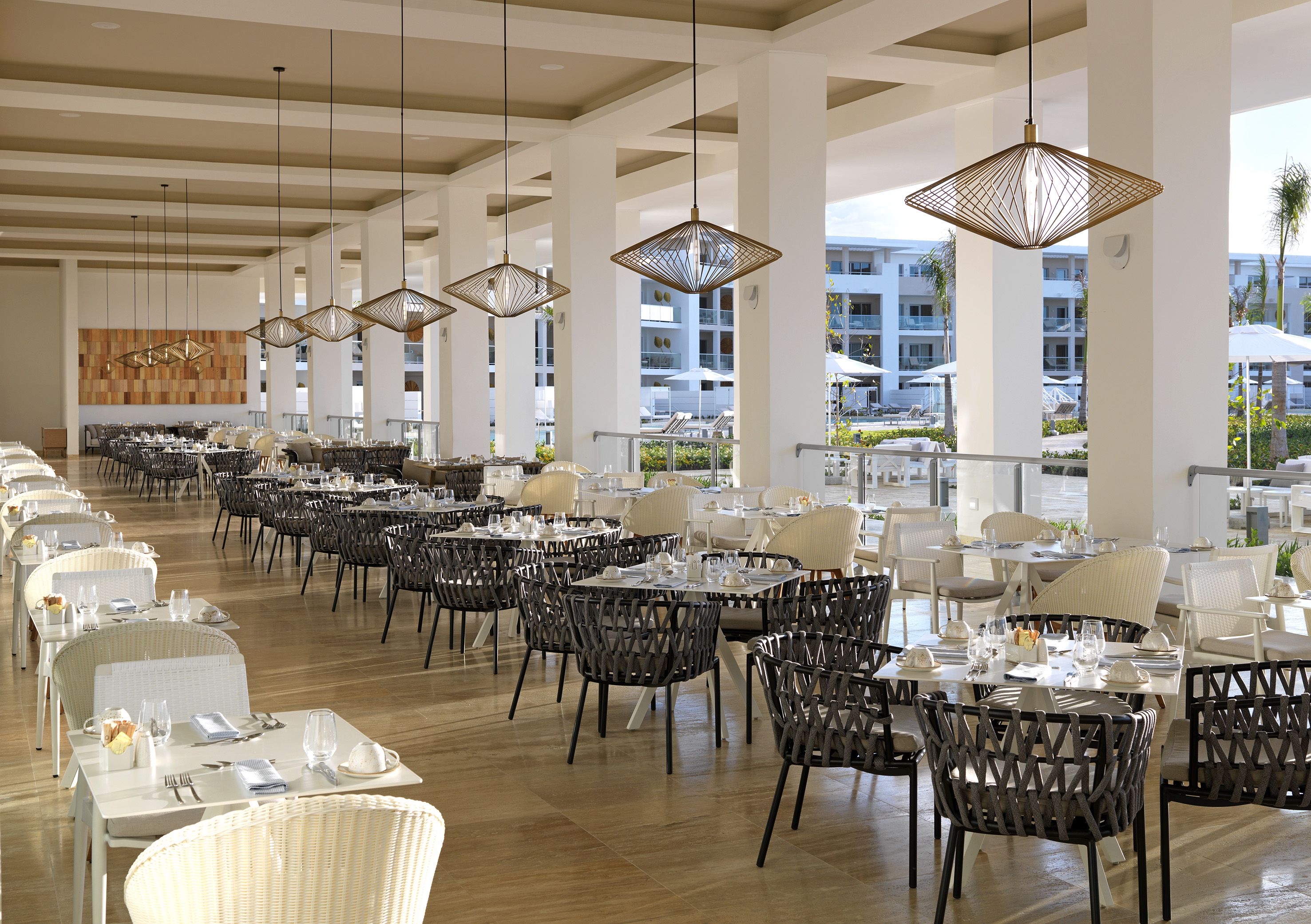 Bright, open-air resort restaurant with modern tables, chairs, and pendant lights.