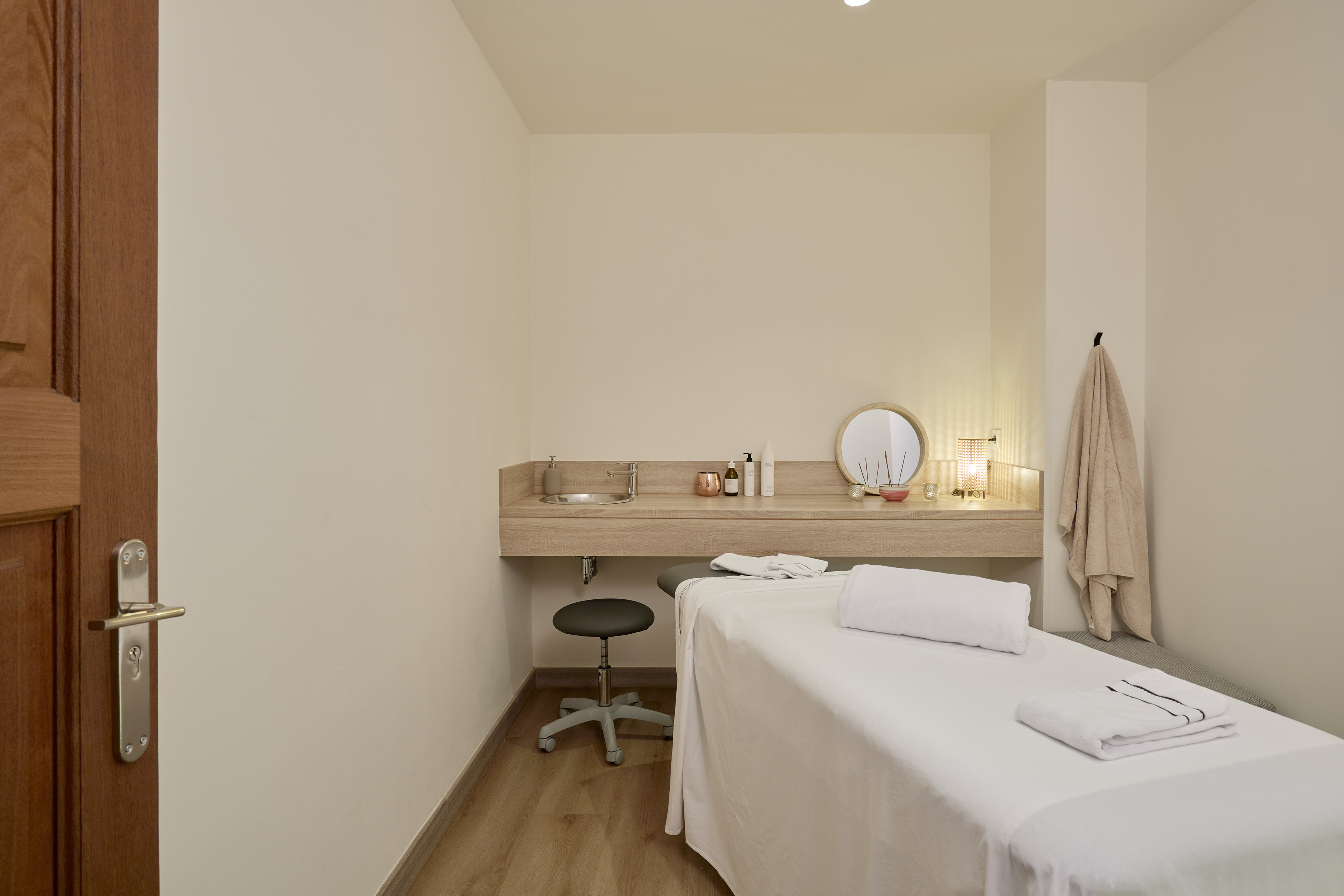 Spa treatment room with white massage bed, sink vanity, and wellness products.