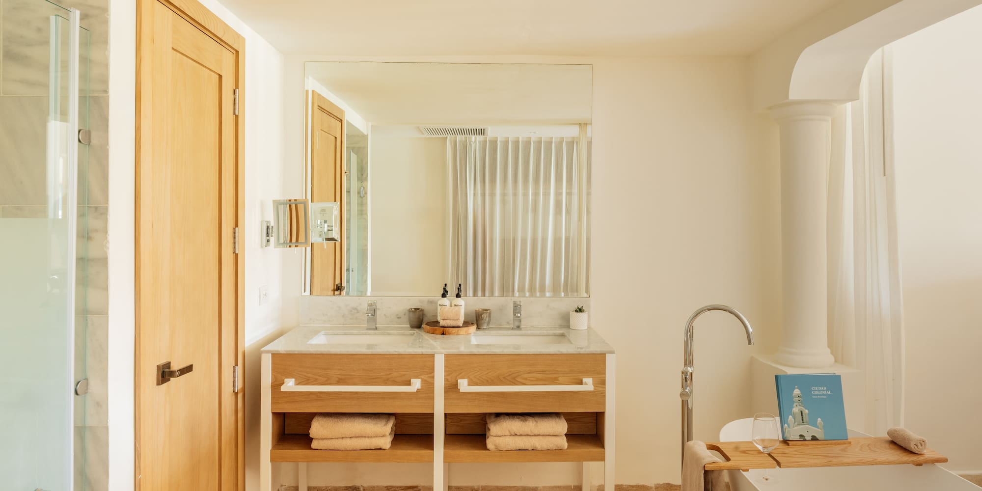Modern bathroom: double marble vanity, wooden base, freestanding tub, shower.
