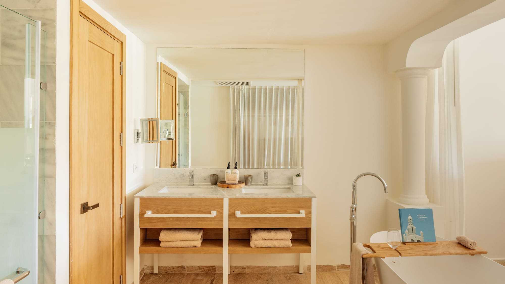Modern bathroom: double marble vanity, wooden base, freestanding tub, shower.