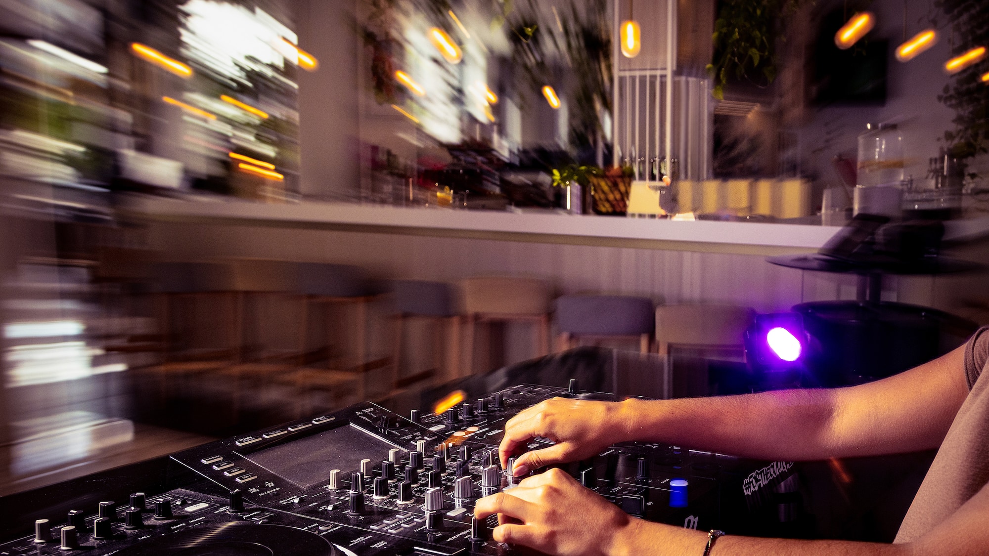 DJ mixing on a controller, hands adjusting knobs, blurry nightclub lights.