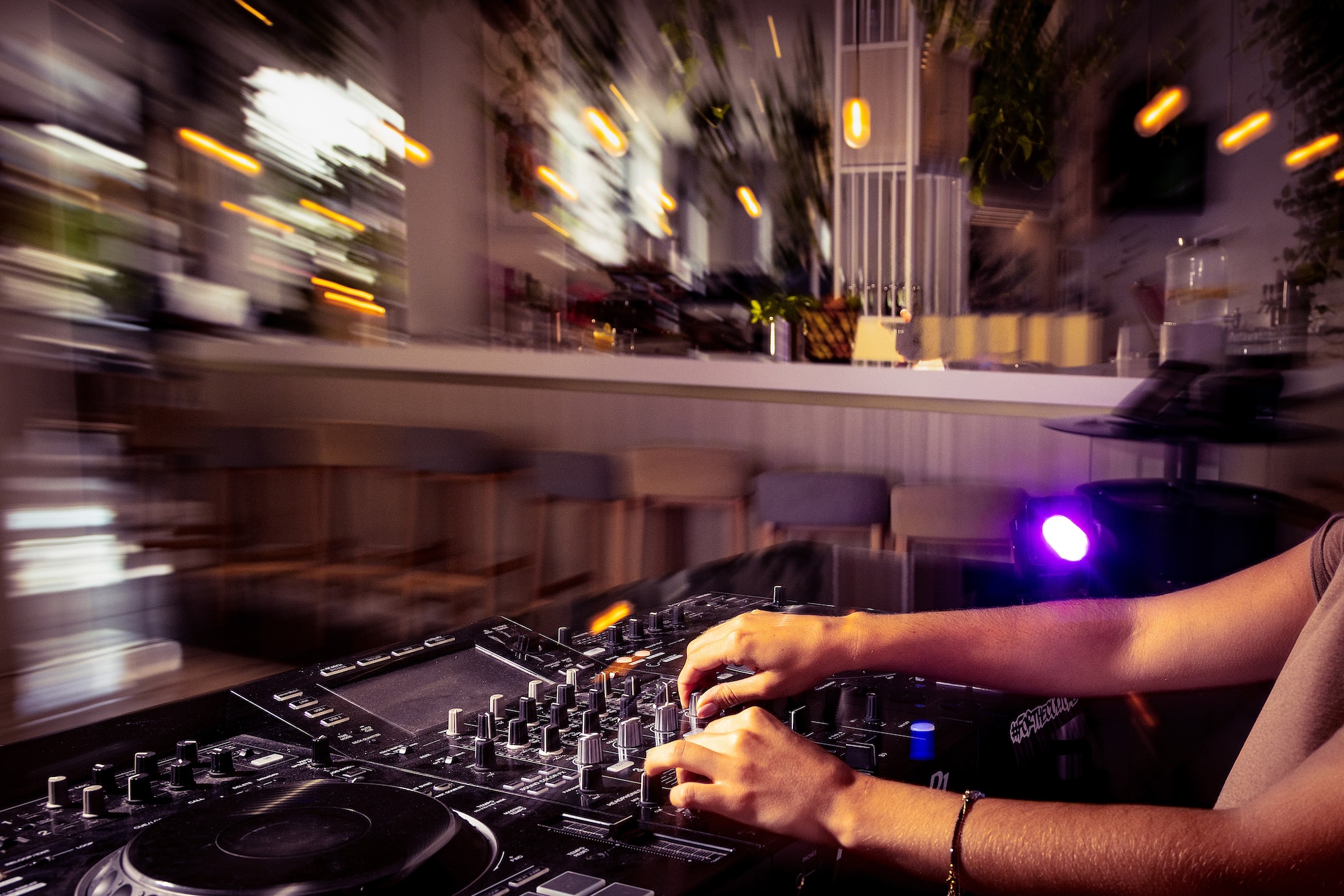 DJ mixing on a controller, hands adjusting knobs, blurry nightclub lights.