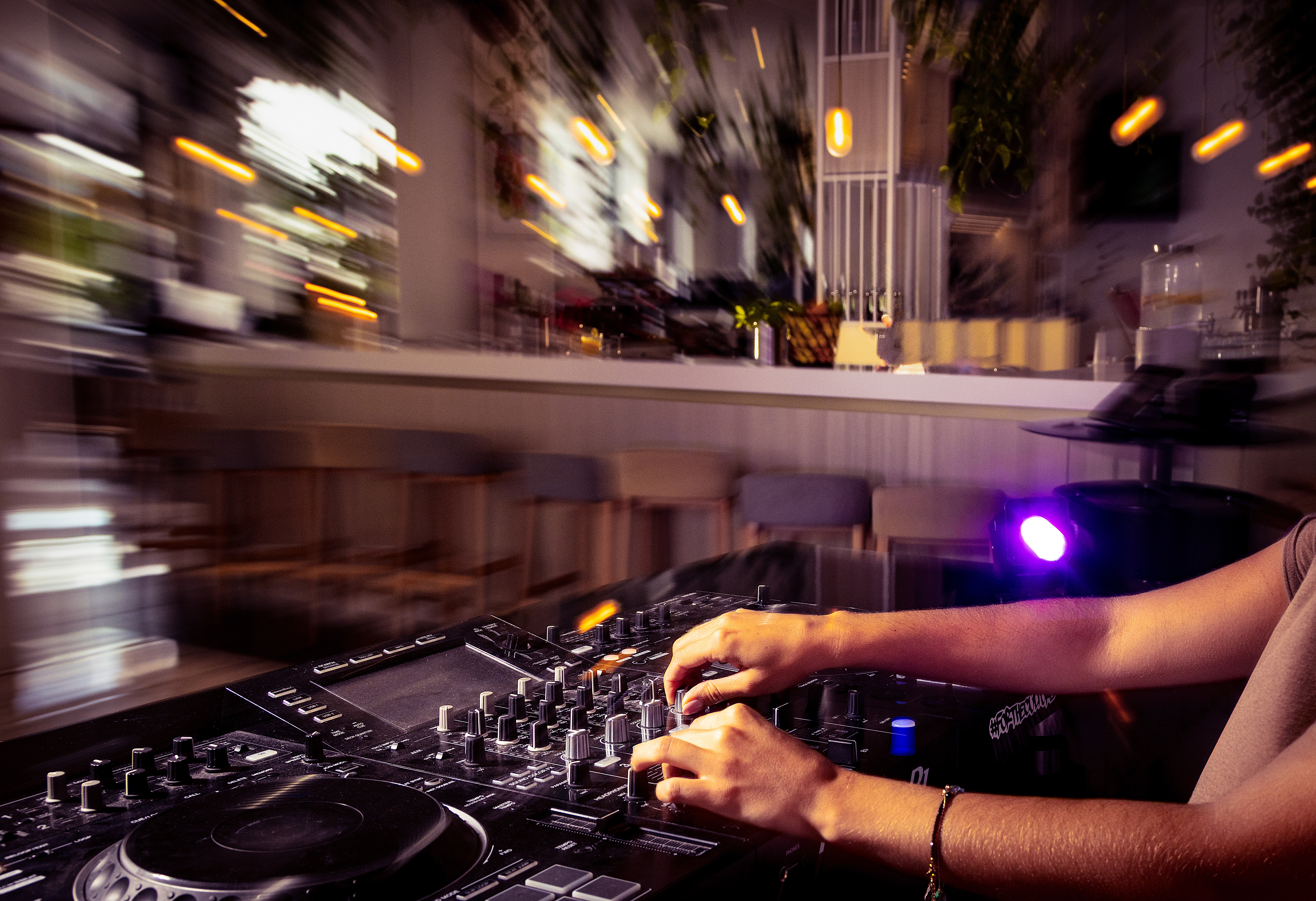 DJ mixing on a controller, hands adjusting knobs, blurry nightclub lights.