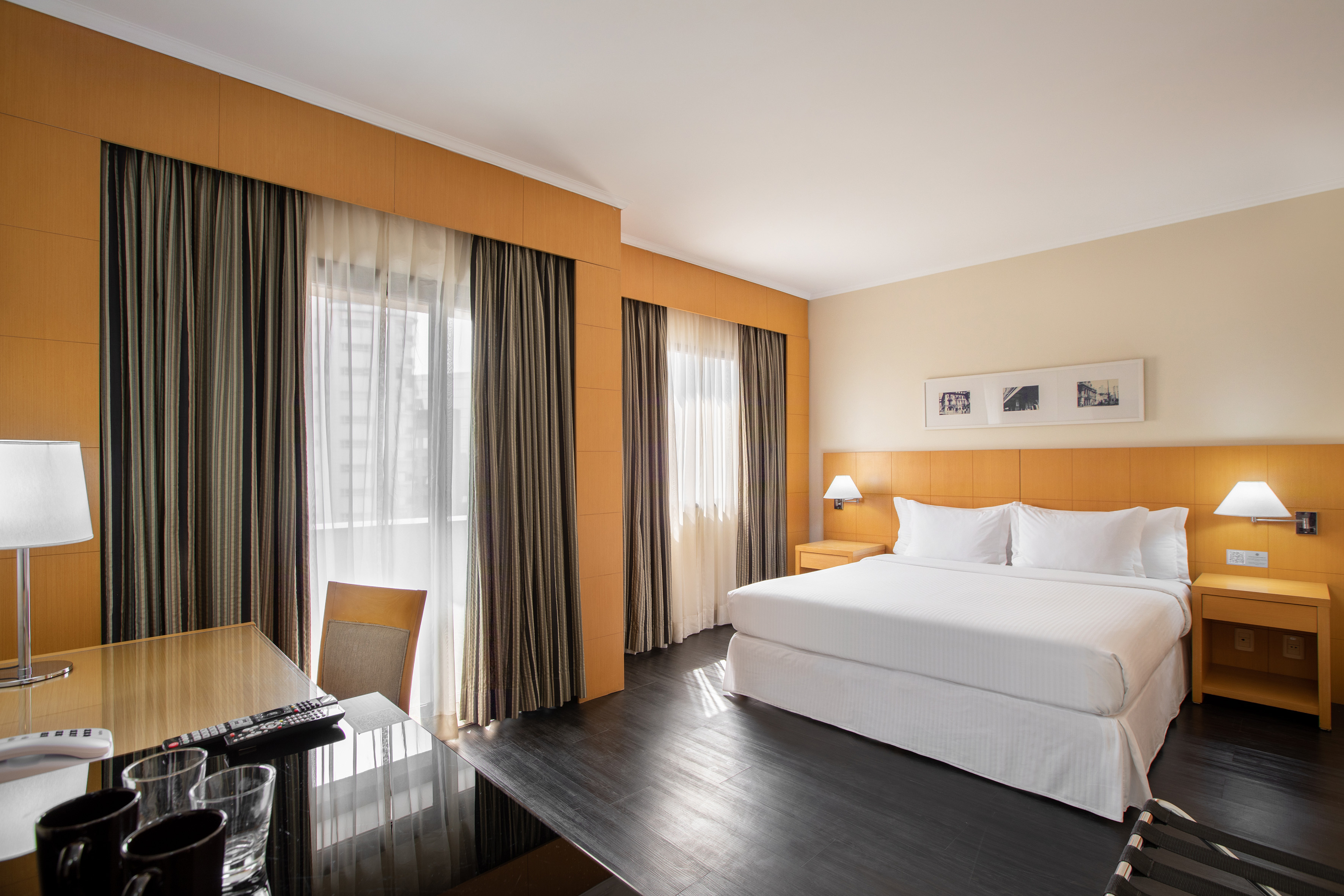 Bright hotel room with king bed, workspace desk, and striped window curtains.