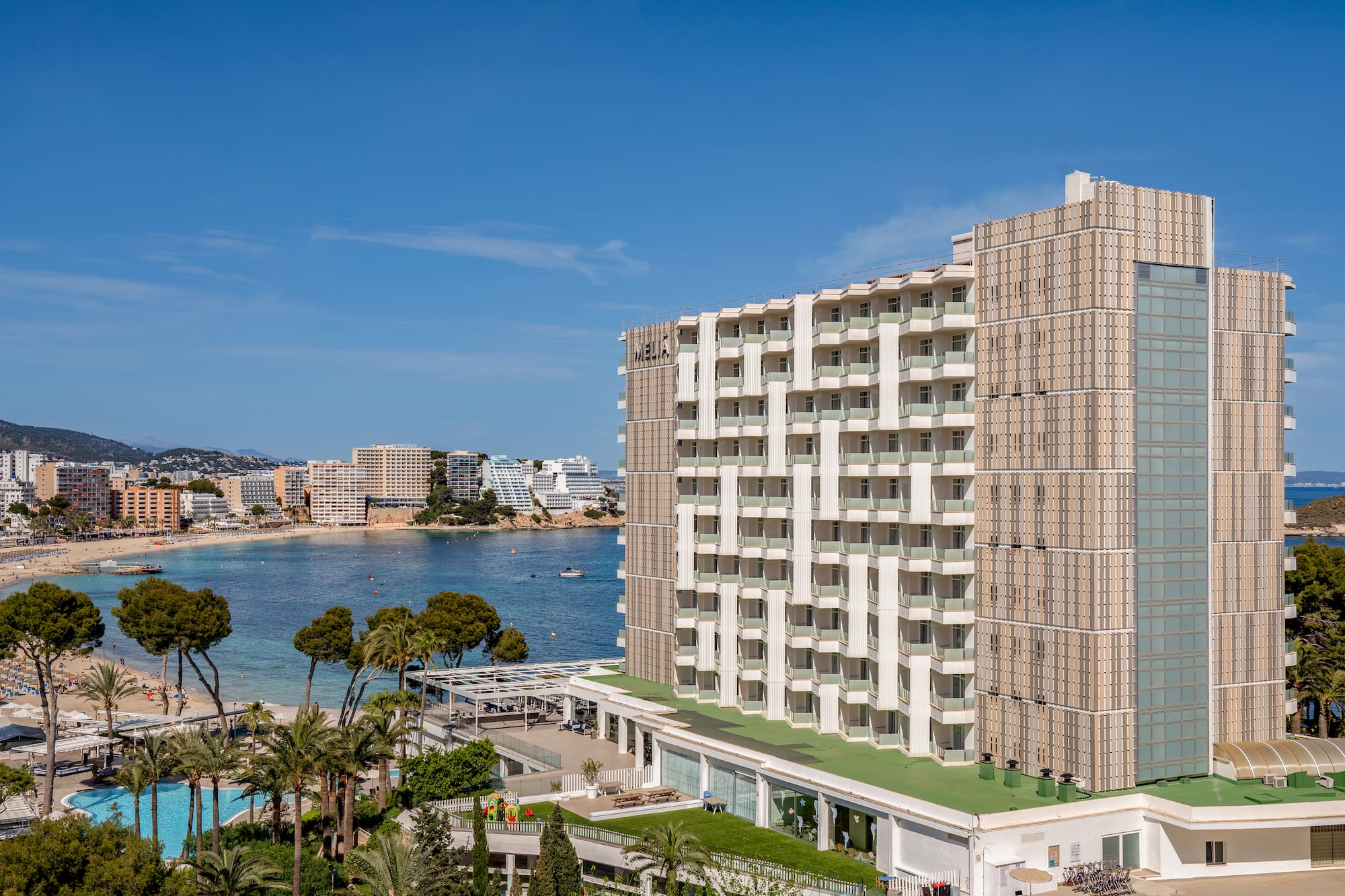 Modern resort hotel with balconies, pool, and sunny bay beach view.