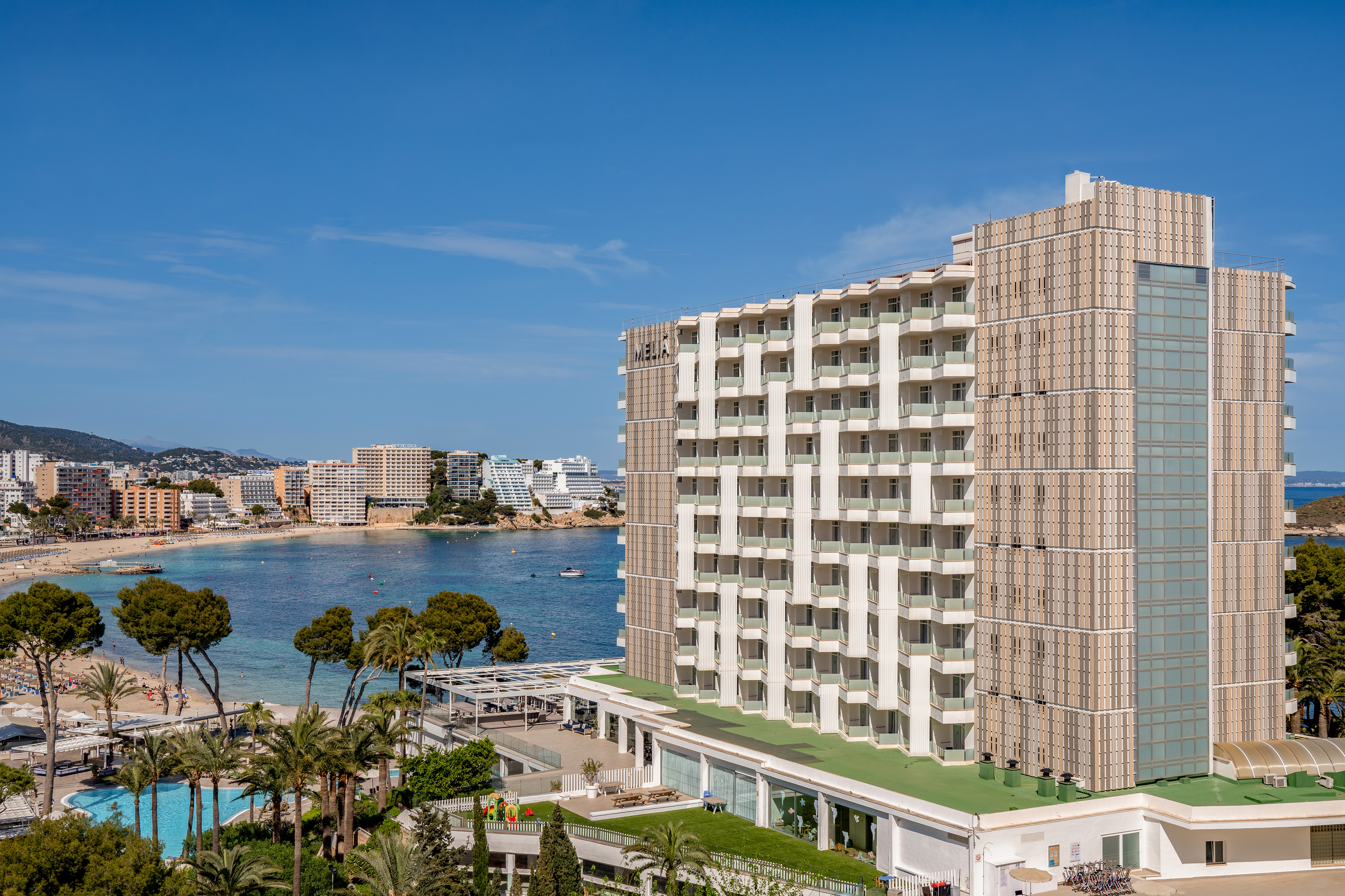 Modern resort hotel with balconies, pool, and sunny bay beach view.