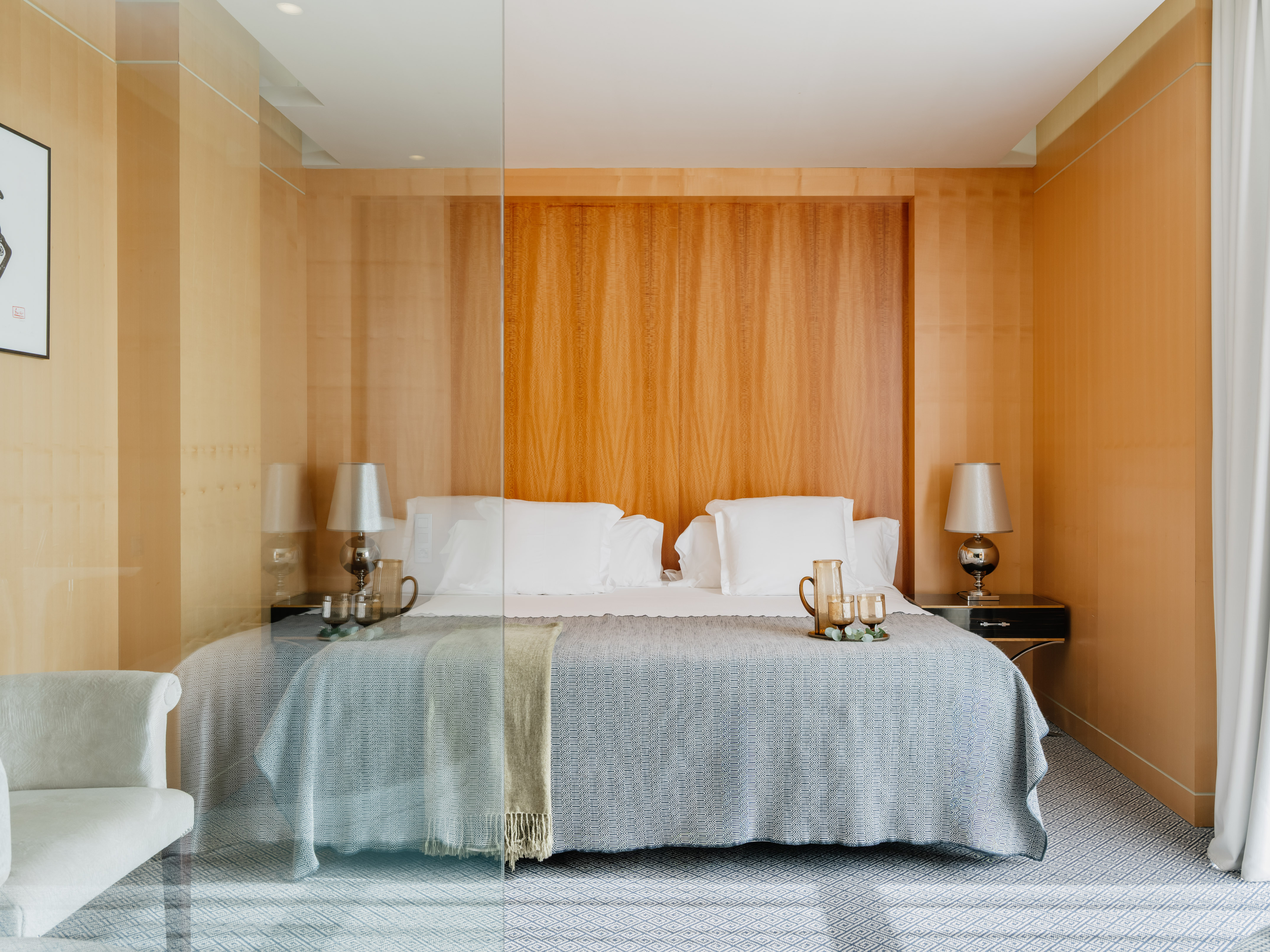Modern wood-paneled bedroom with bed, patterned blanket, and glass partition.