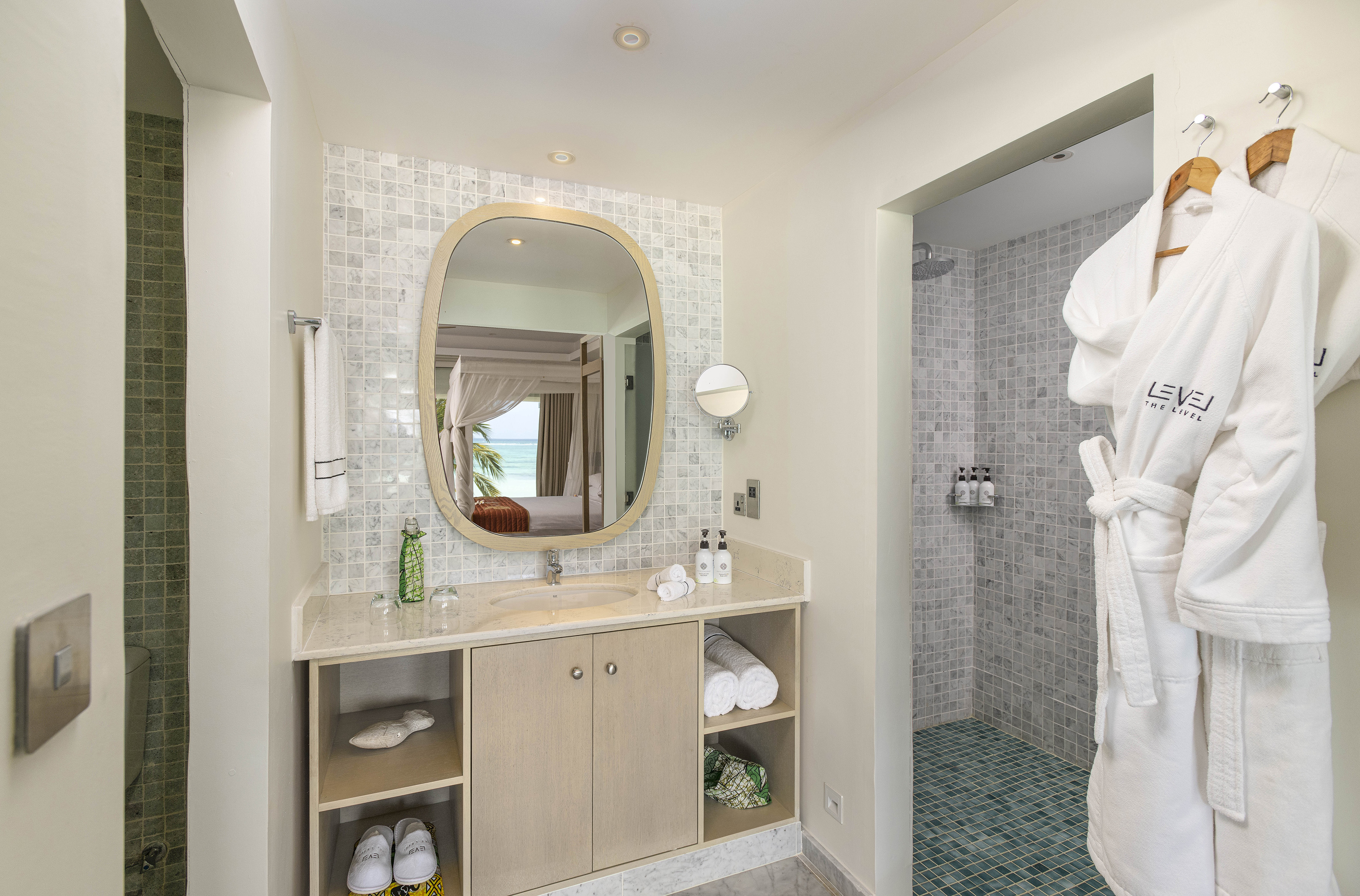 Luxury hotel bathroom with modern vanity, shower, and ocean view reflected in mirror.