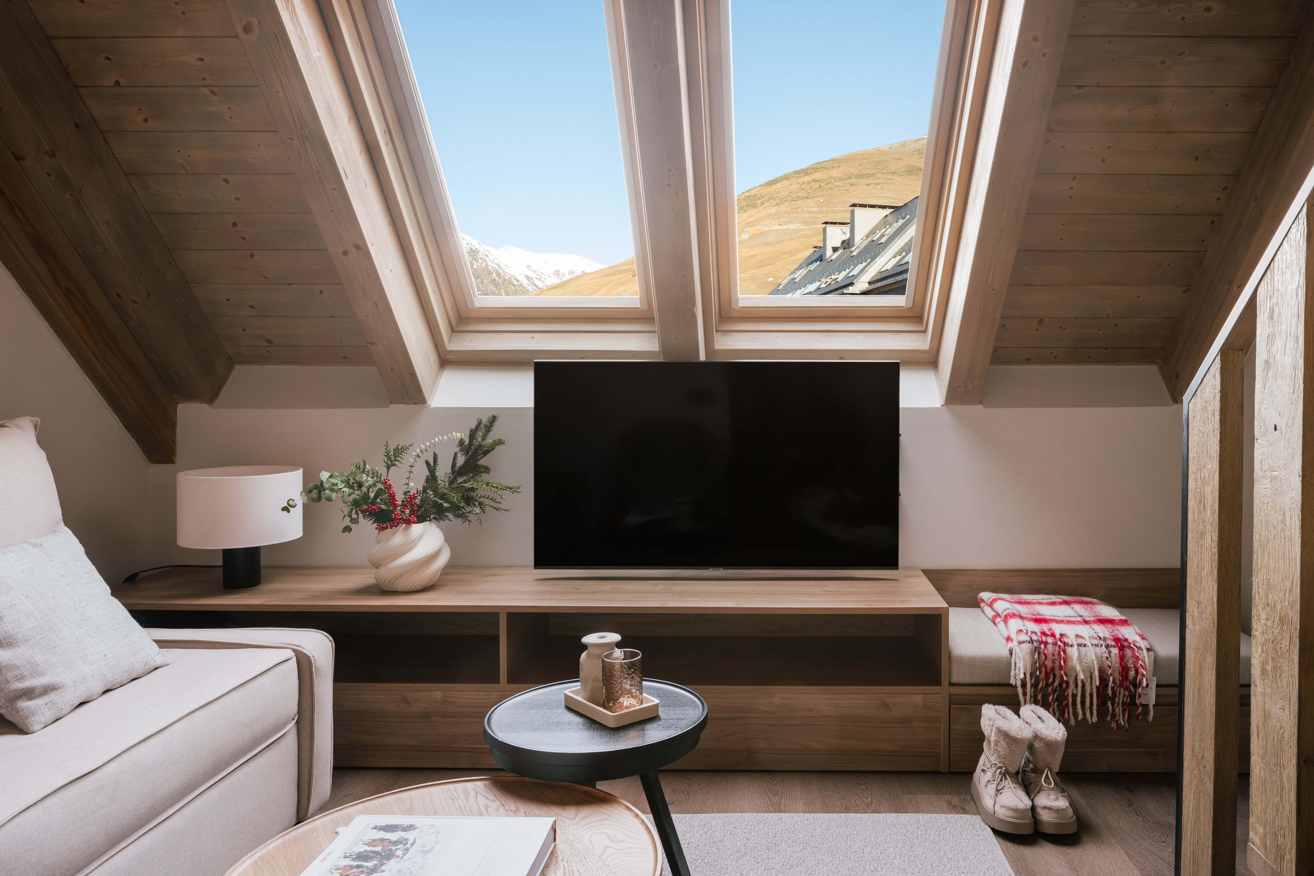 Cozy loft living room with mountain view through skylights, TV, and wooden decor.