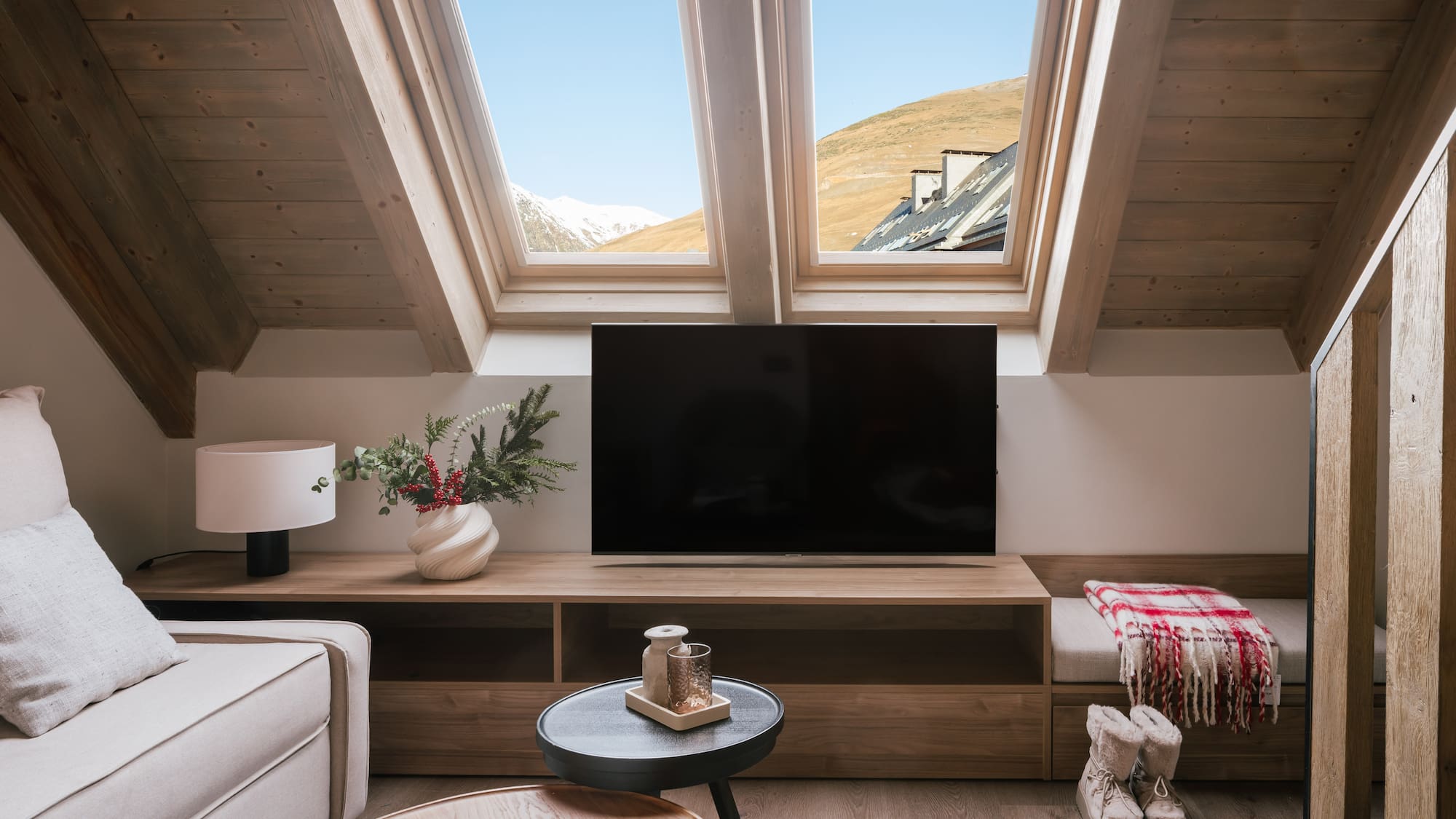 Cozy loft living room with mountain view through skylights, TV, and wooden decor.