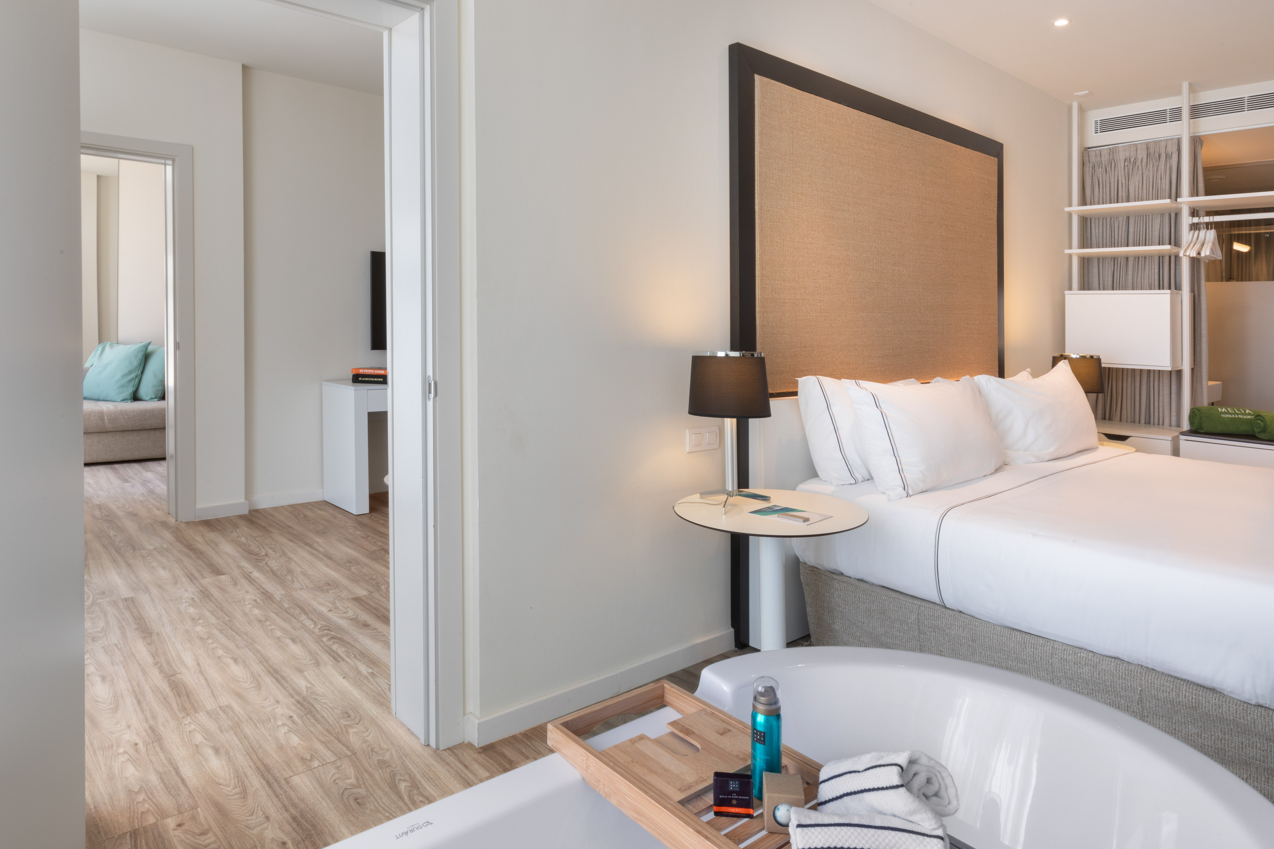 Modern hotel room with white bed, open-concept bathtub, and light wooden floor.